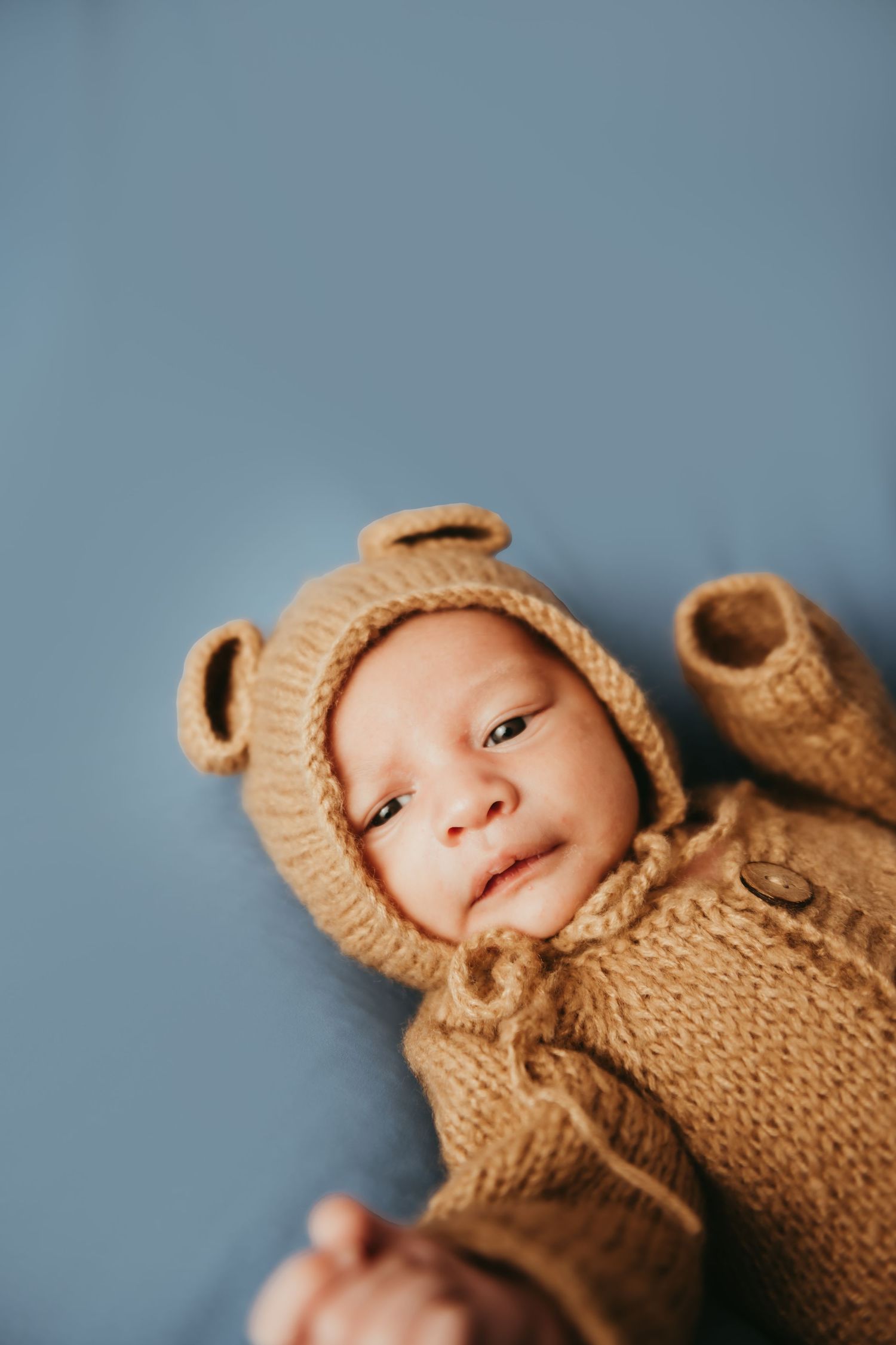 Newborn baby wearing a cozy brown knitted bear outfit with ears, lying on a soft blue background.