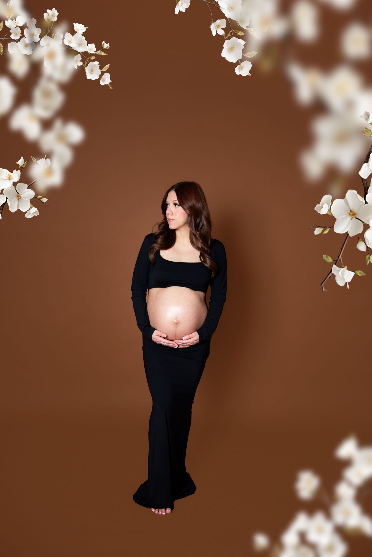 Maternity photoshoot with white cherry blossoms against brown backdrop.