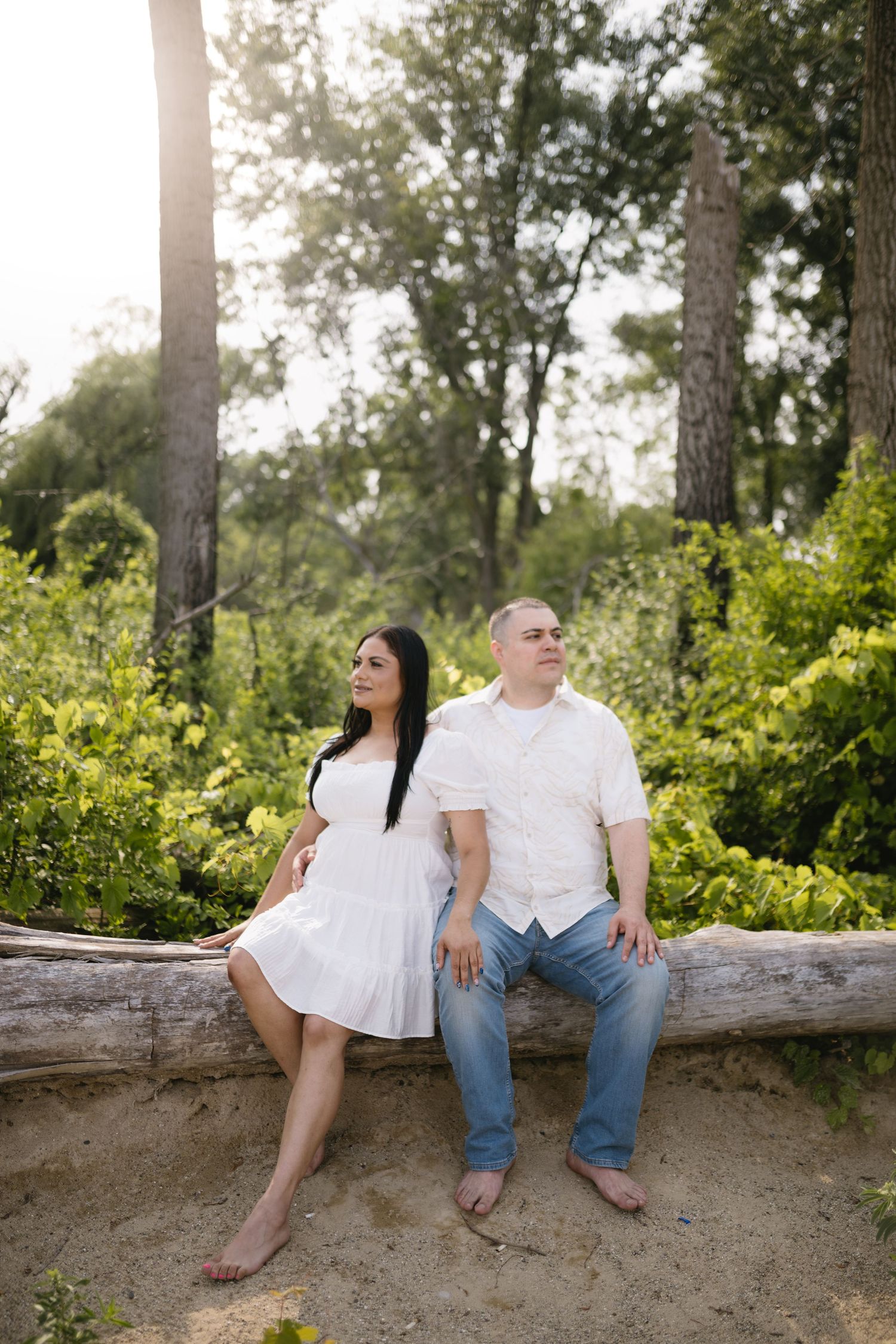 Couple sitting together on fallen log surrounded by lush greenery.
