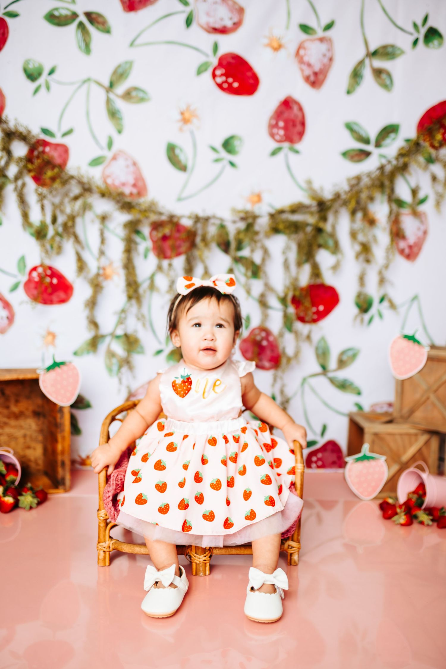Strawberry-themed first birthday photo setup with floral backdrop and pink decor.