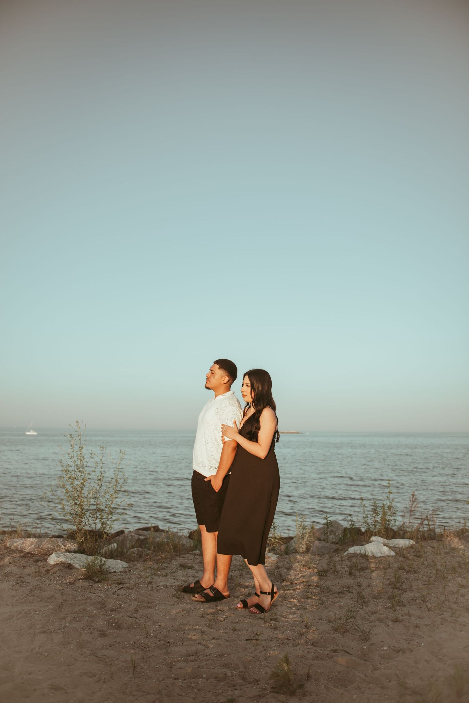 Couple stands together overlooking ocean horizon at sunset.