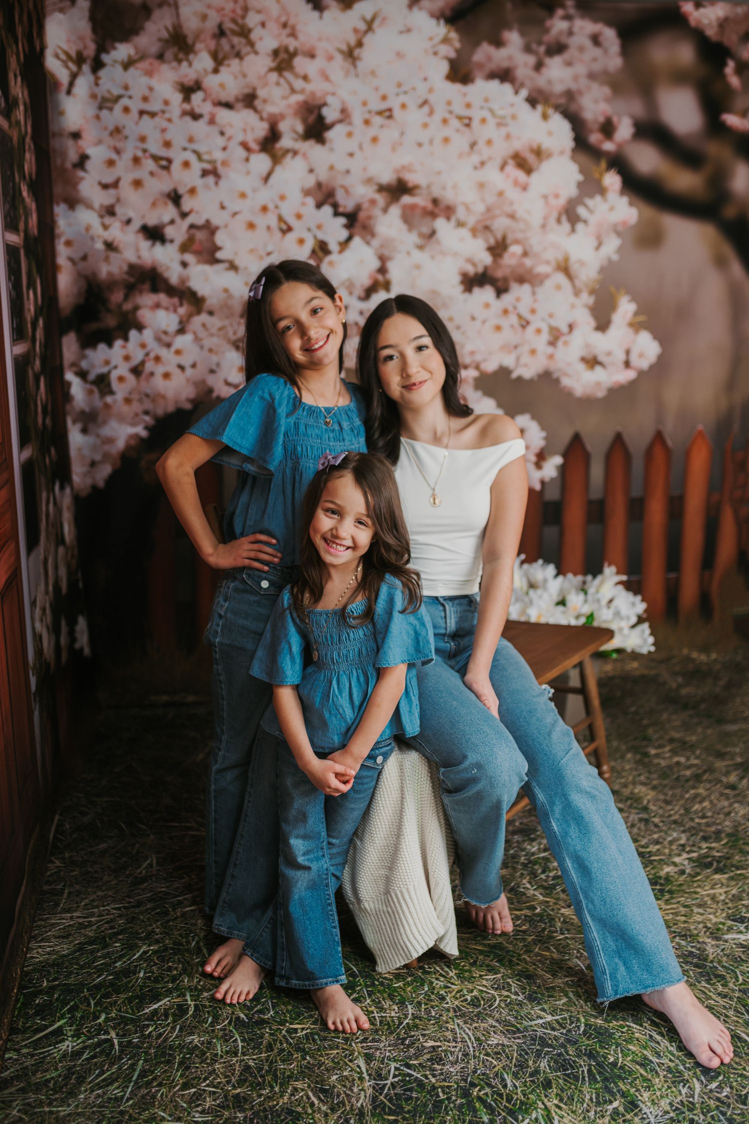 Casual family photo shoot under pink cherry blossoms with wooden fence backdrop.