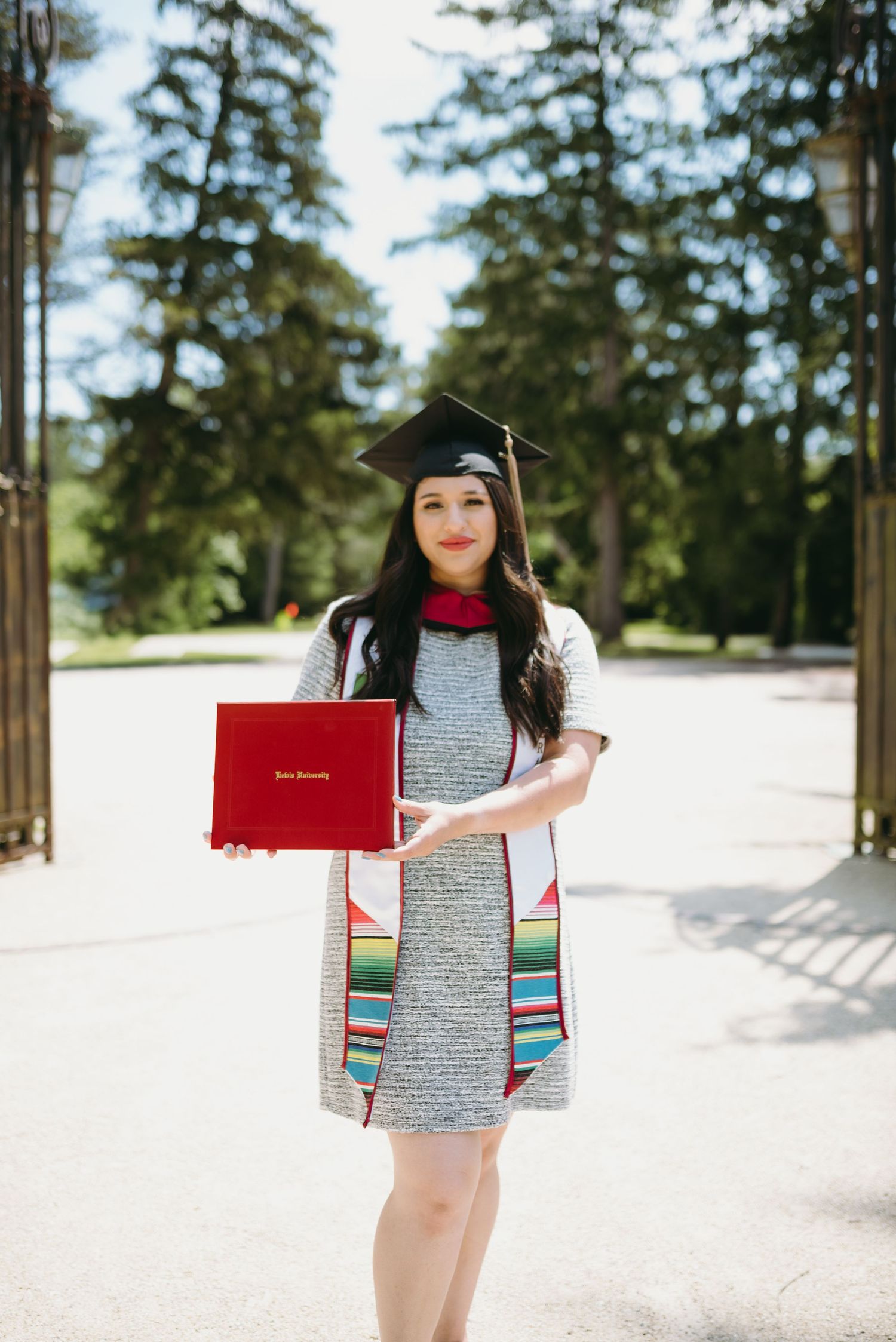 Graduate in cap and gown poses with diploma in snowy pine forest setting.