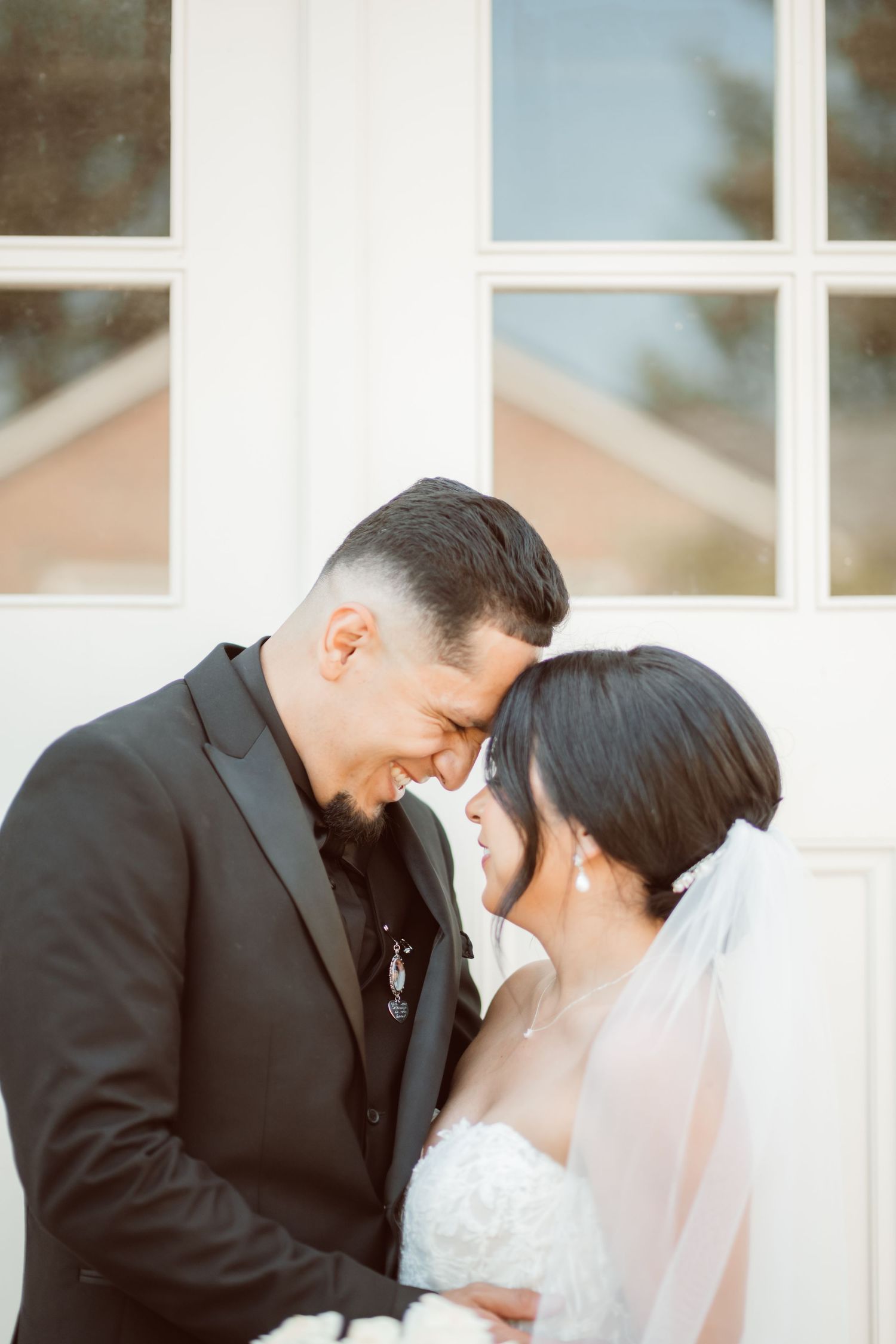 Romantic outdoor wedding portrait against white building exterior.