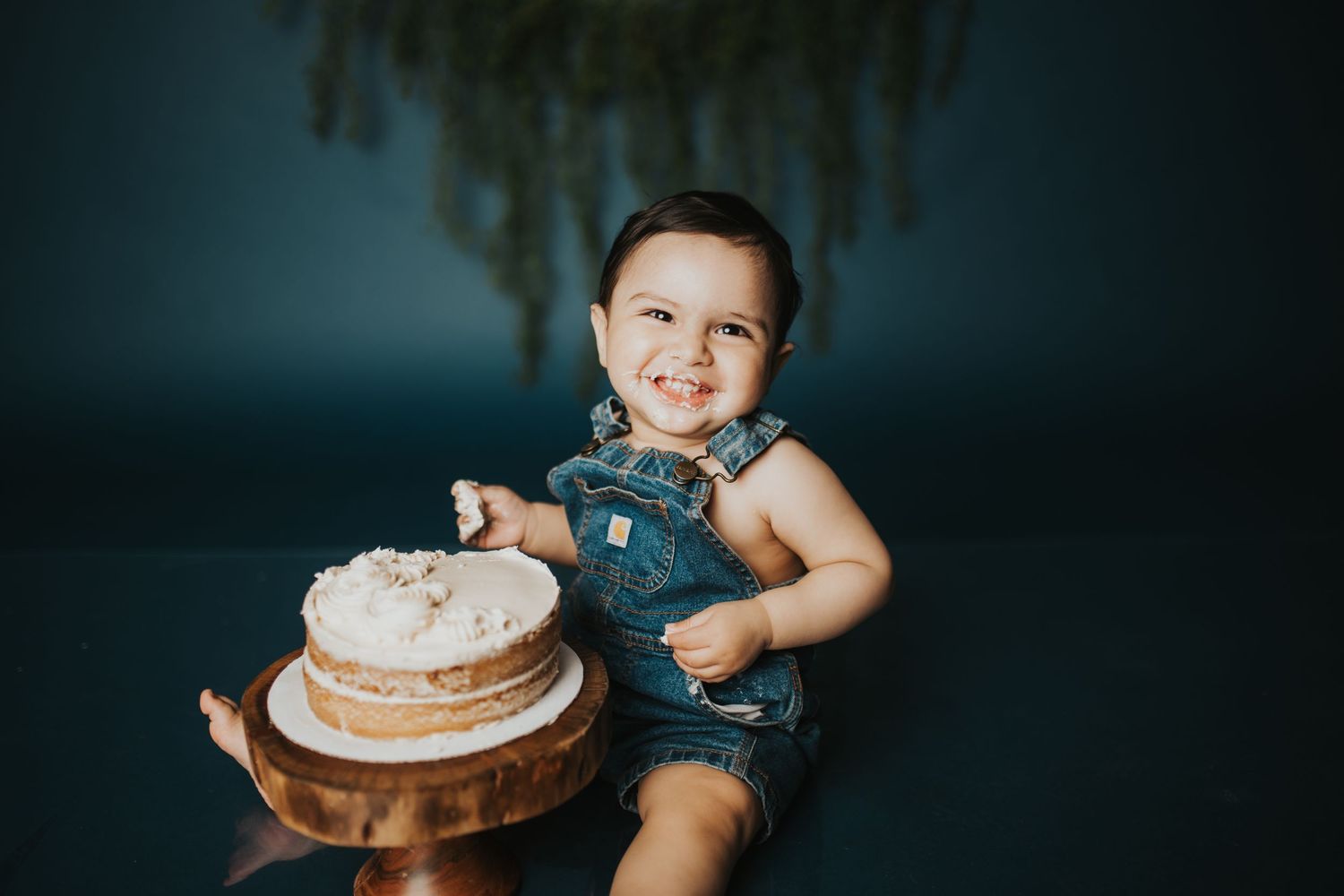 Cake smash photography session with dark blue backdrop and rustic decor.