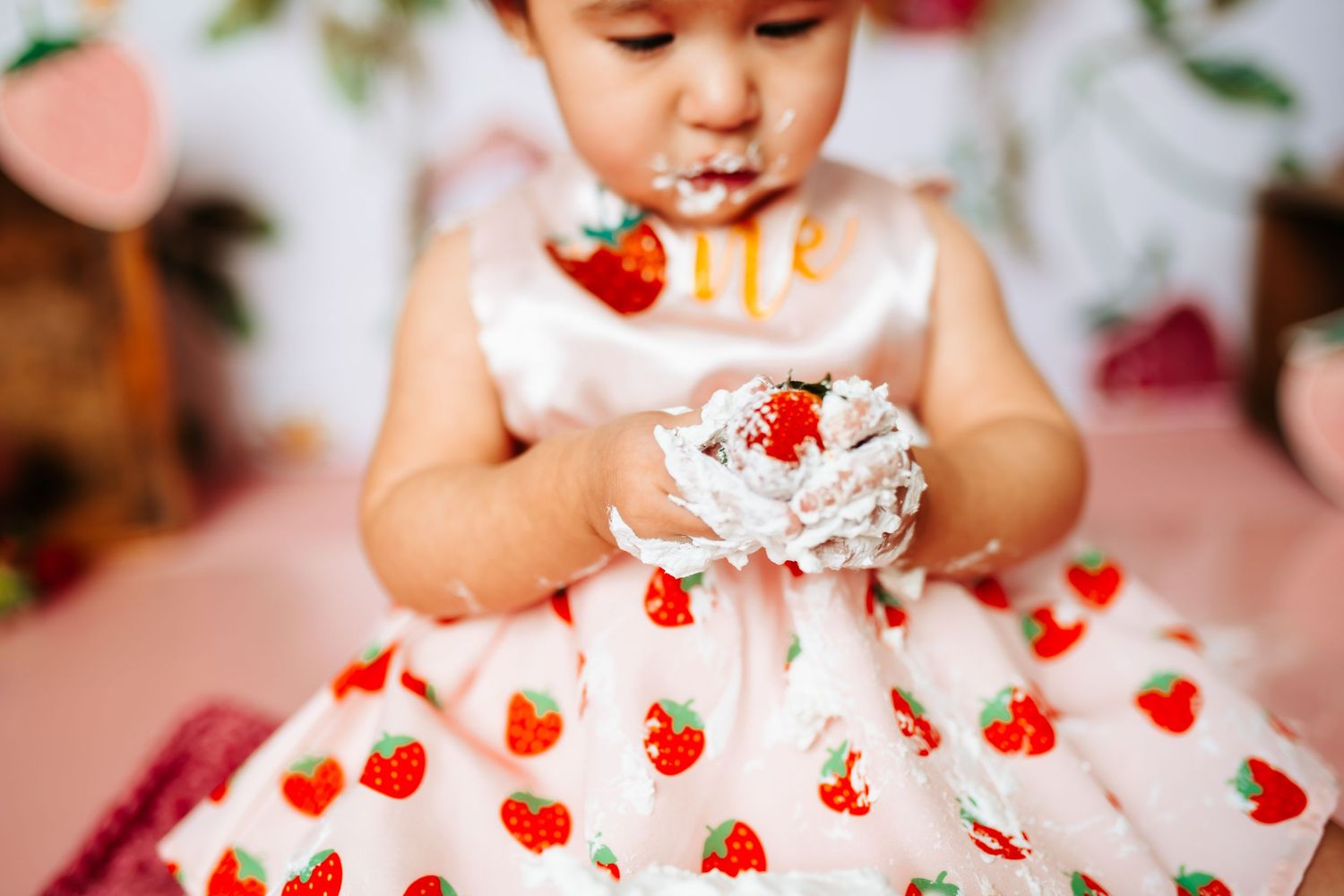 Close-up of strawberry print dress during cake smash photo session.
