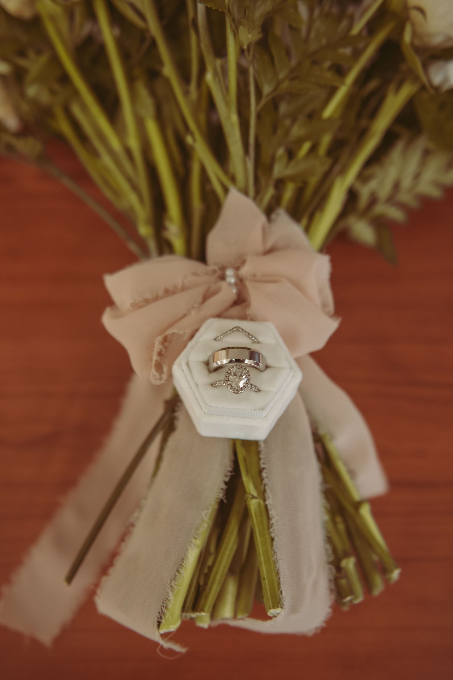 Wedding rings displayed on a flower bouquet stem wrap with delicate ribbon details.
