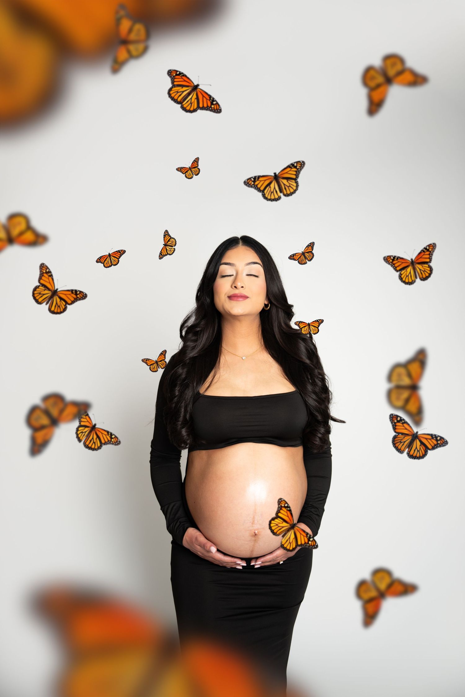 Maternity portrait with orange monarch butterflies floating around in white studio setting.