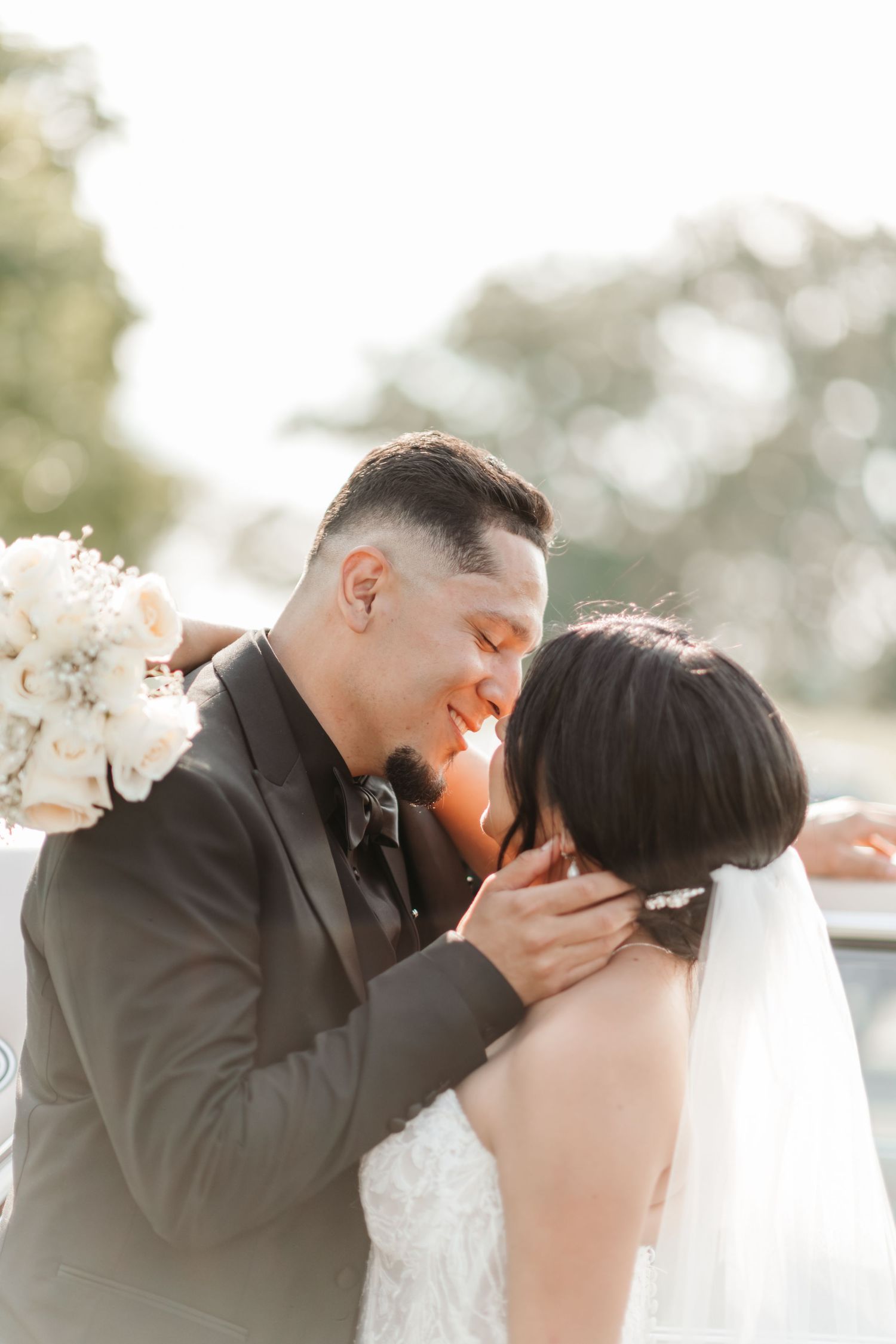 Intimate wedding moment captured in soft sunlight with a flowing white veil and bouquet.