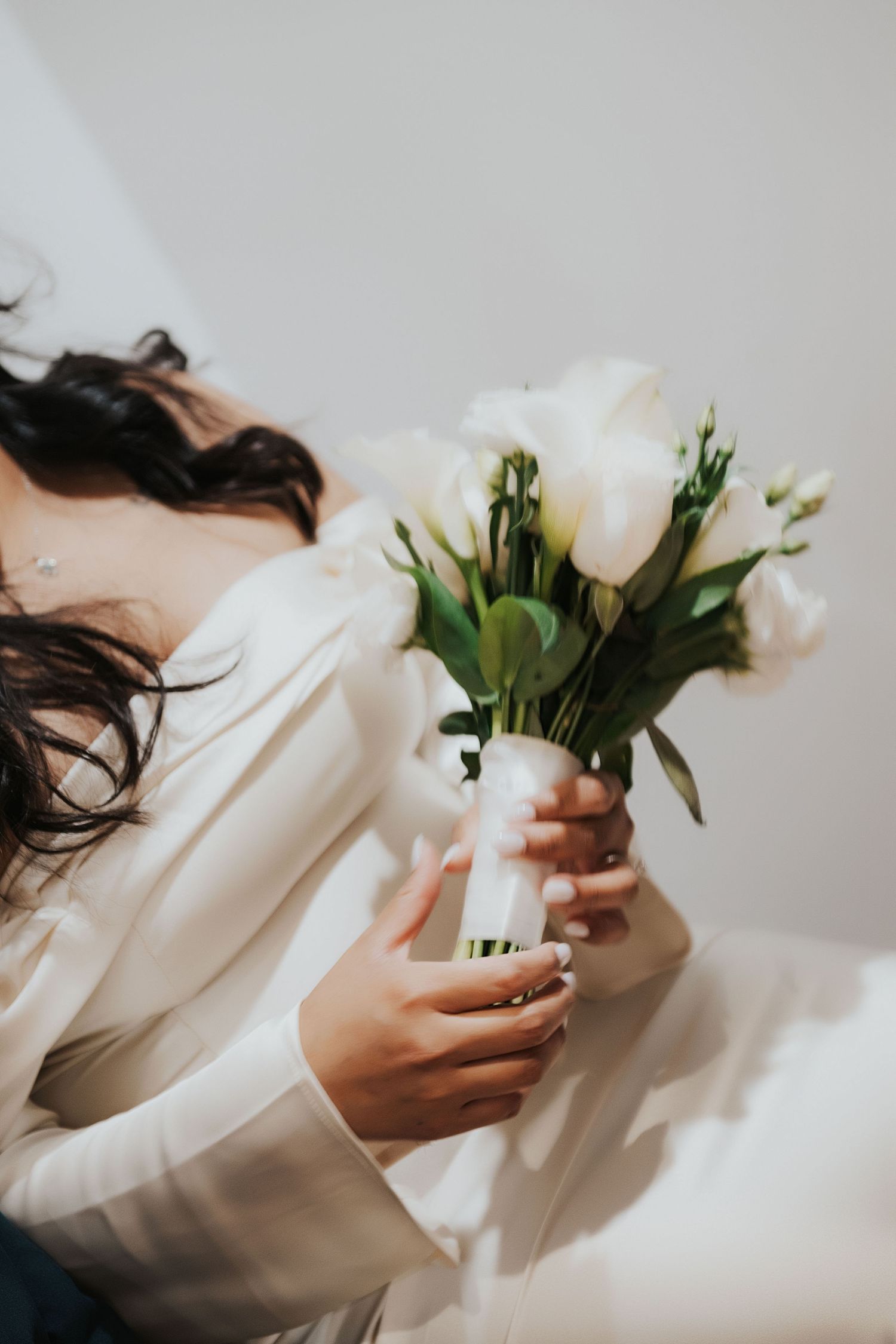 Hands holding elegant white roses and greenery against white background.
