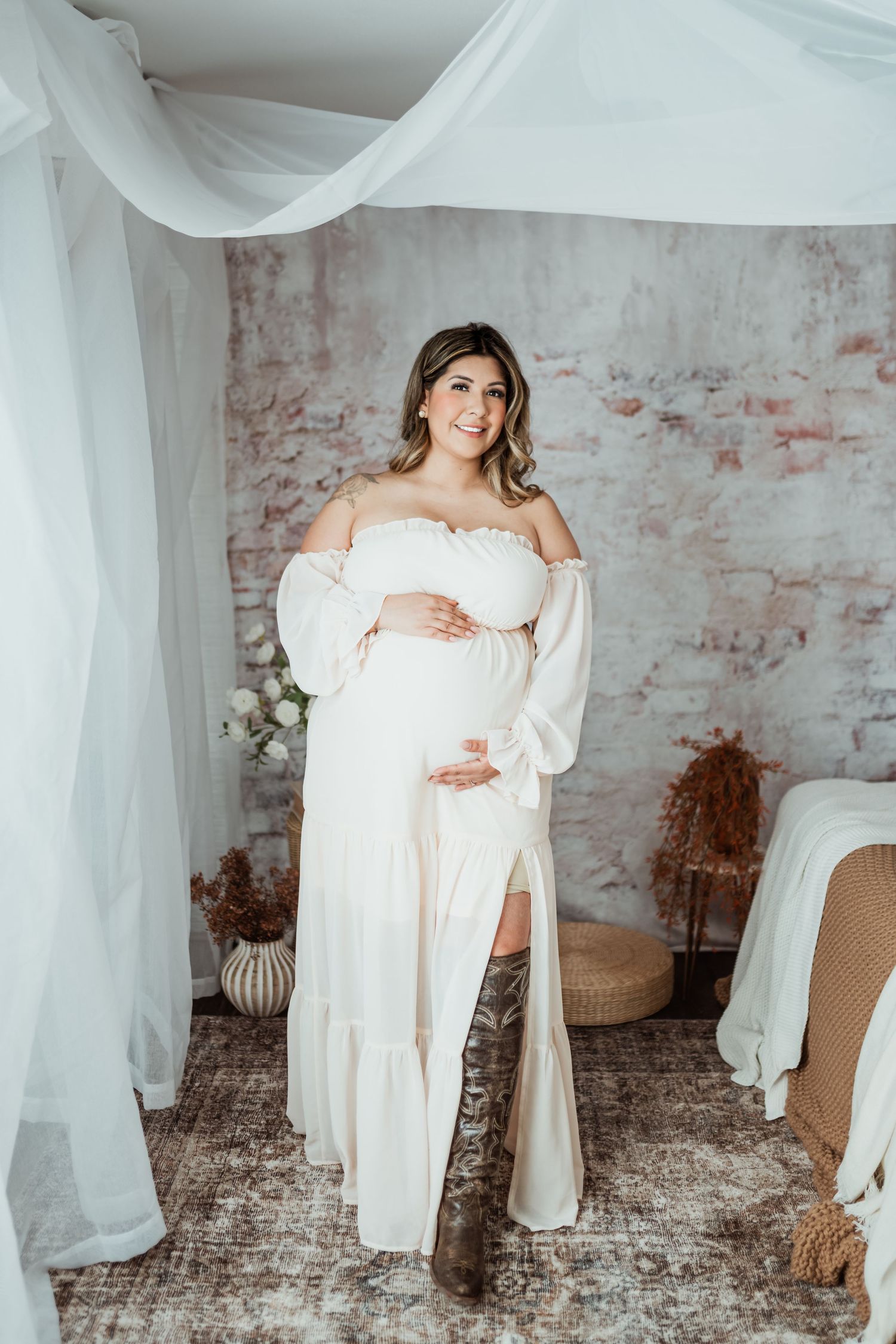 Maternity portrait in white off-shoulder dress against vintage brick wall.