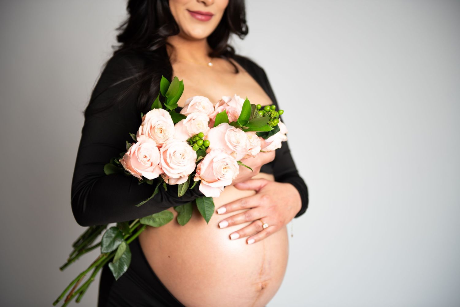 Elegant maternity photo with pink roses held against white background.