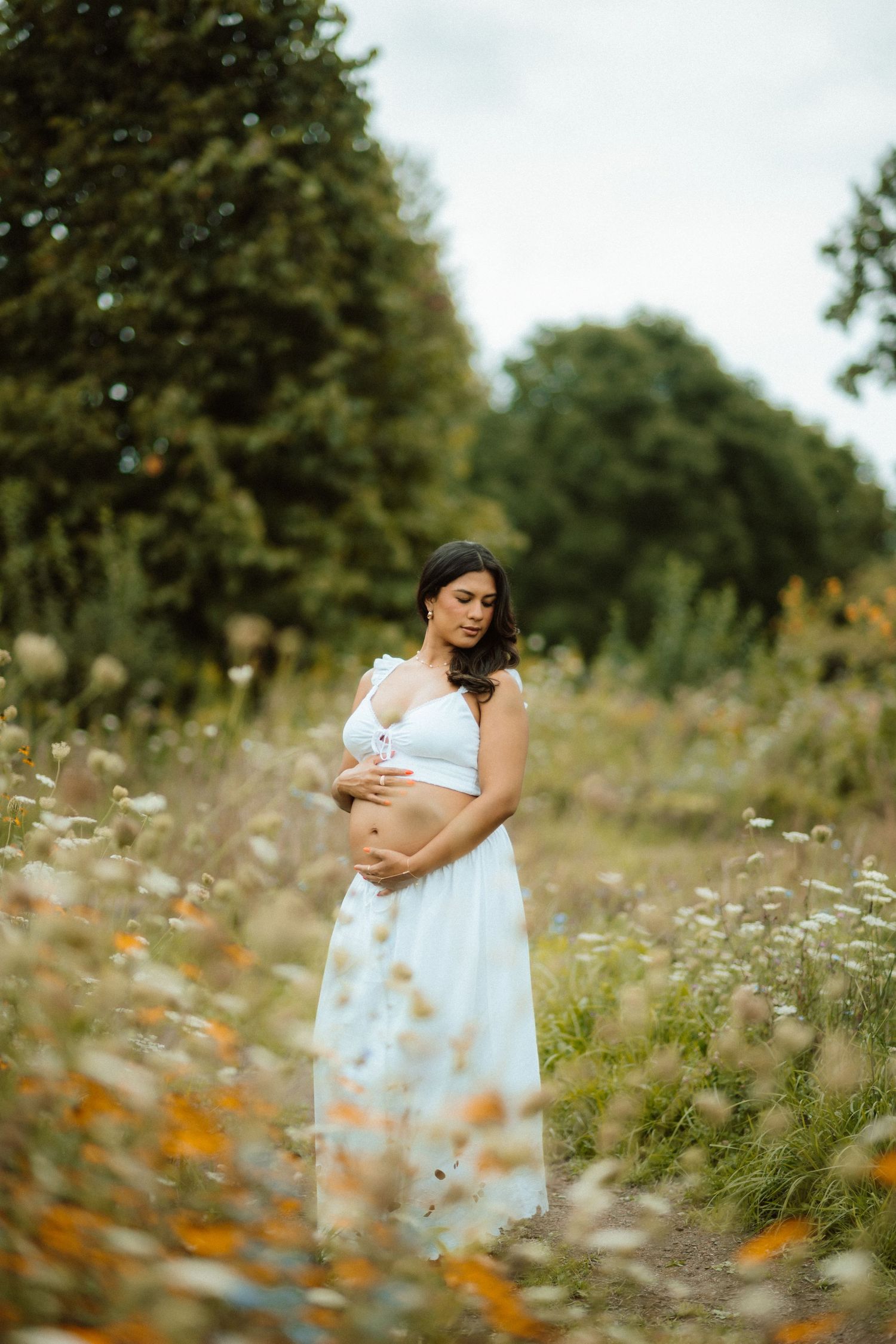 Person in white dress stands among wildflowers in a dreamy outdoor meadow setting.
