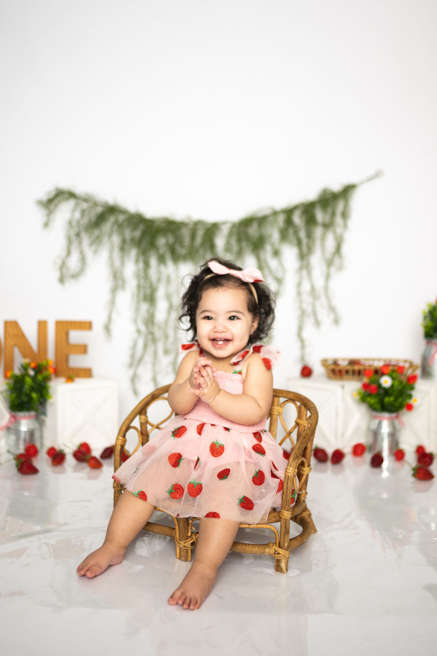 Toddler in polka dot dress sitting on wicker chair with floral party decorations.