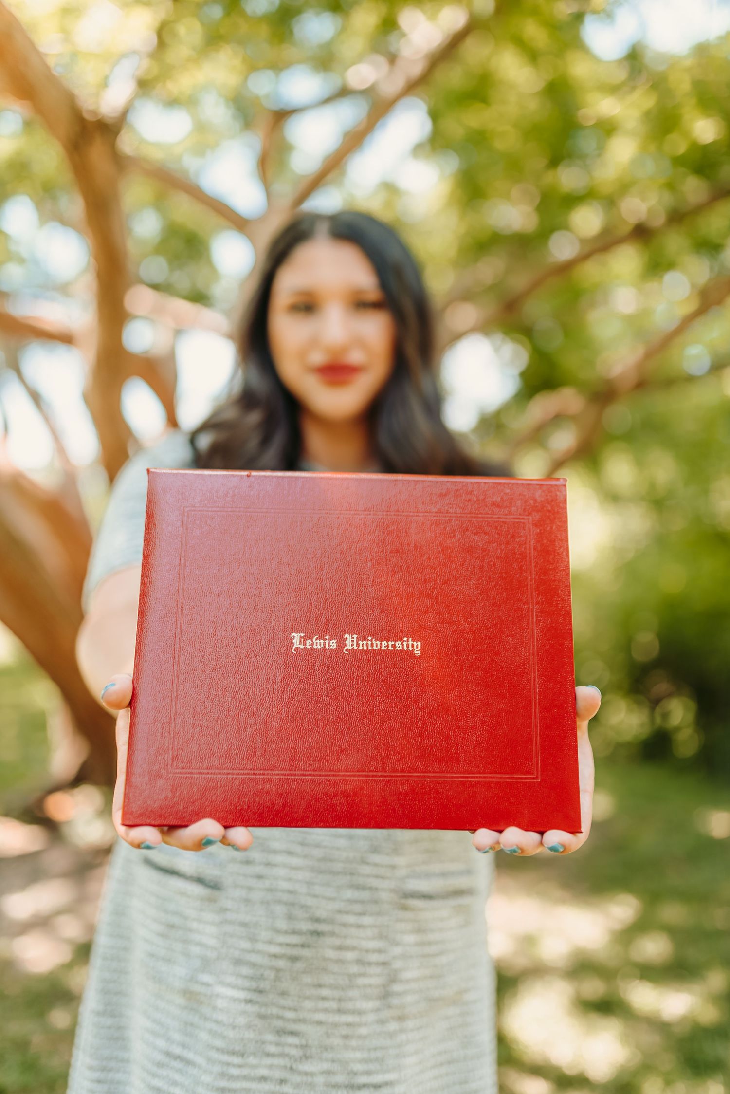 Red diploma held up against grey dress in outdoor graduation photo.