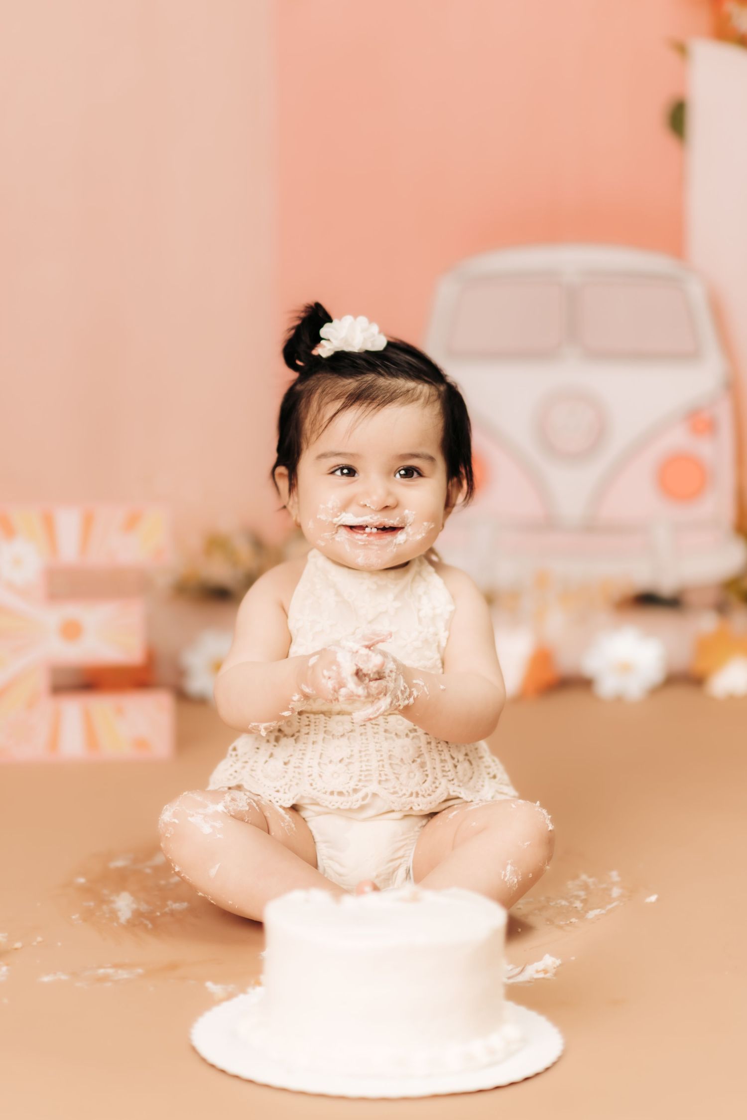 Cake smash photo session with baby in pink outfit and white cake.