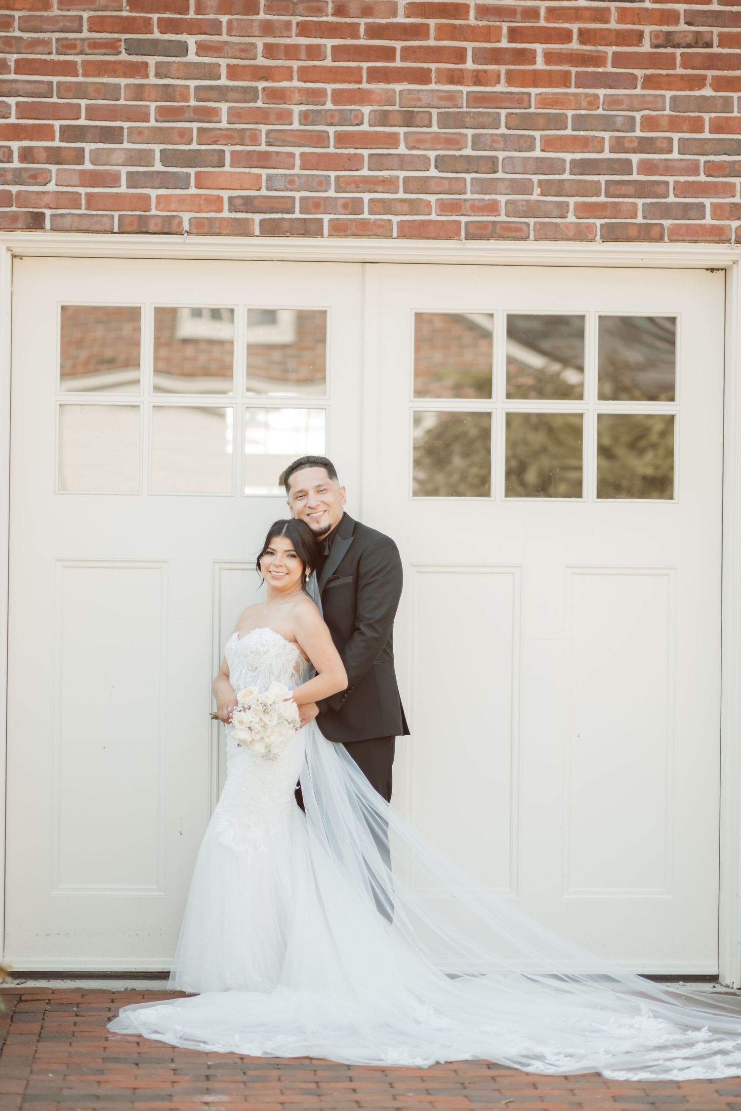 A romantic wedding photoshoot in front of a brick wall and white garage doors with a flowing white dress and veil.