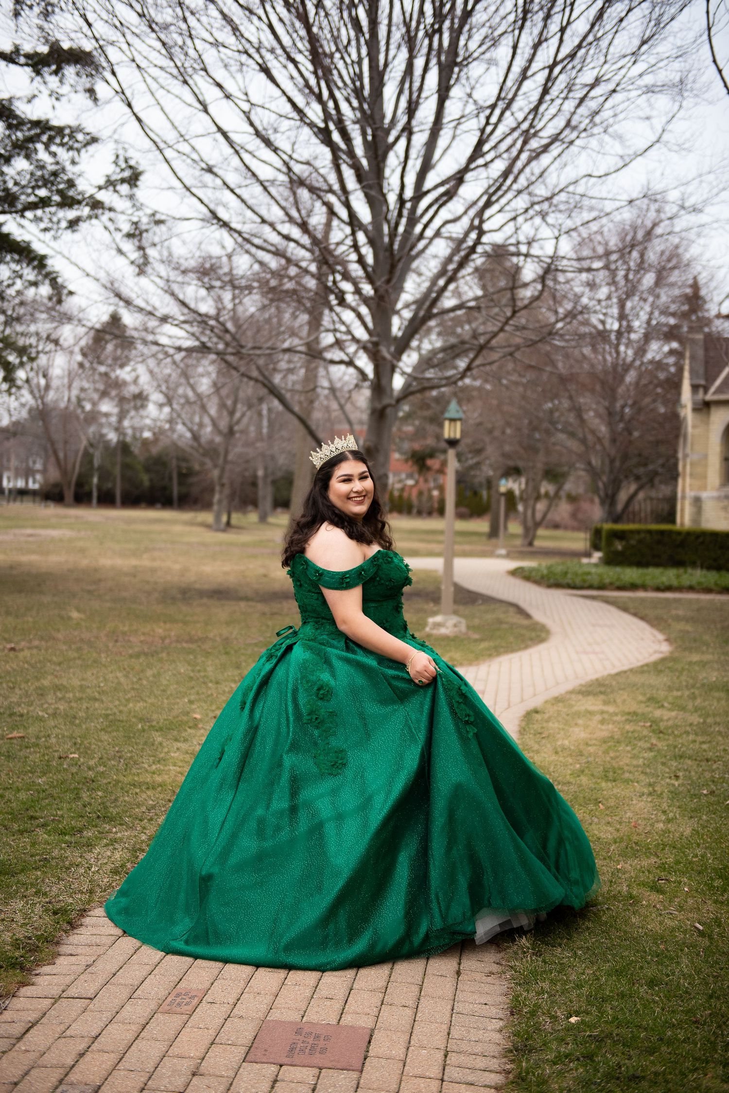 Emerald green ball gown photographed on winding pathway through park setting.
