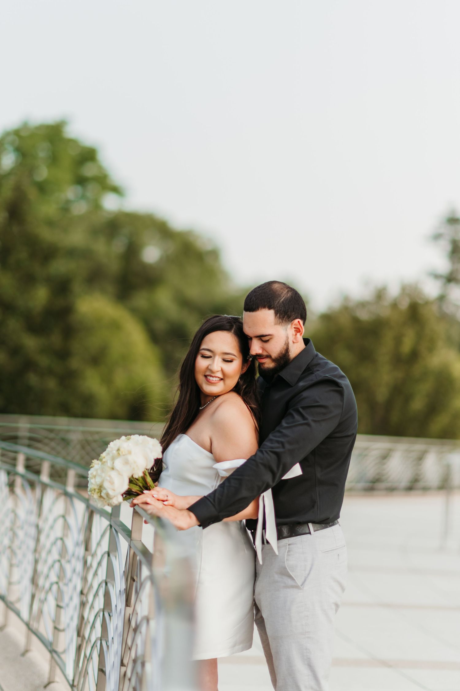 A couple shares romantic poses along an outdoor railing with soft natural lighting.