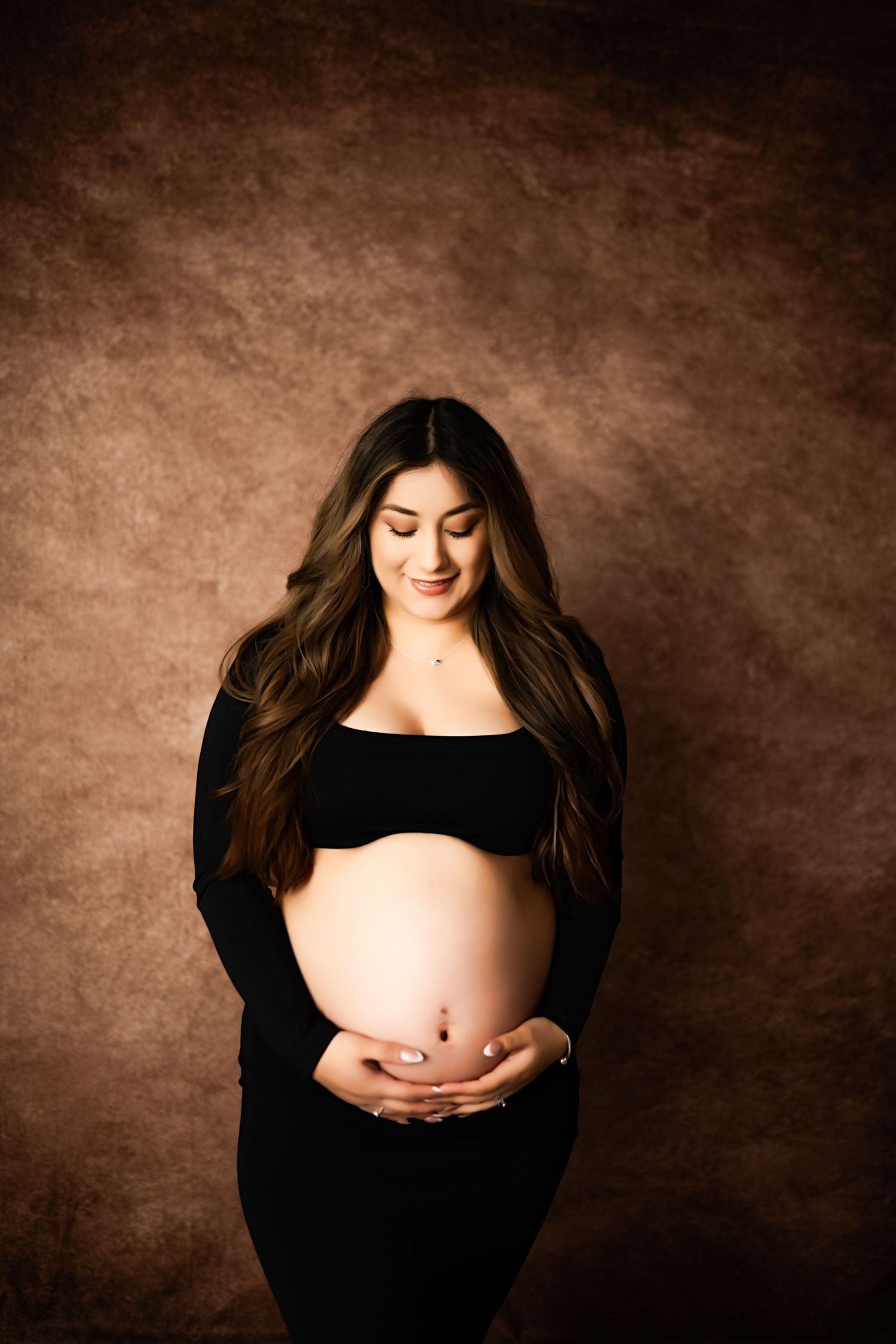 Elegant maternity portrait against brown backdrop in black outfit.