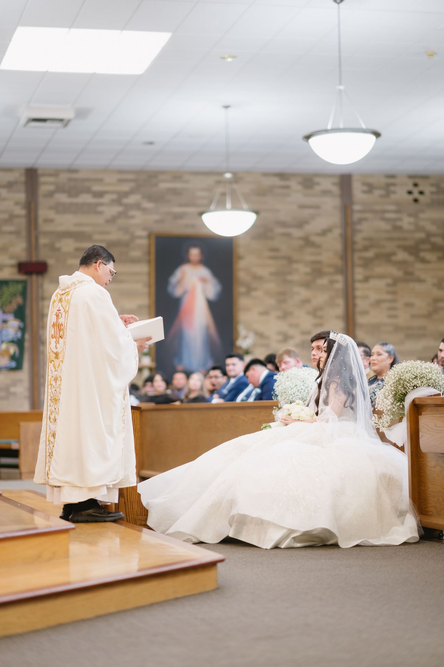 Traditional Catholic wedding ceremony taking place in a church with stone walls and religious artwork.
