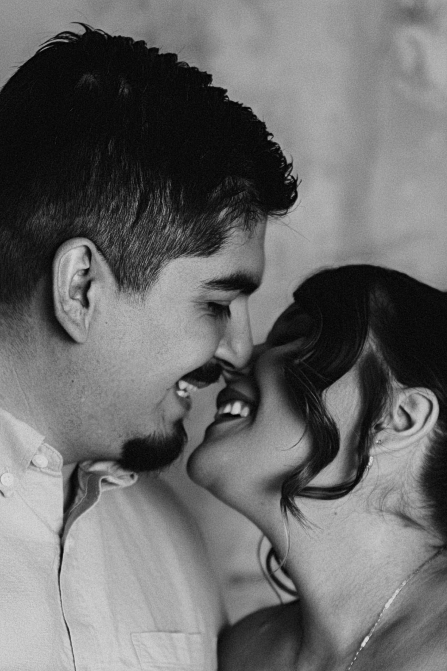 Black and white intimate portrait of a couple sharing a romantic moment, smiling and touching foreheads together.