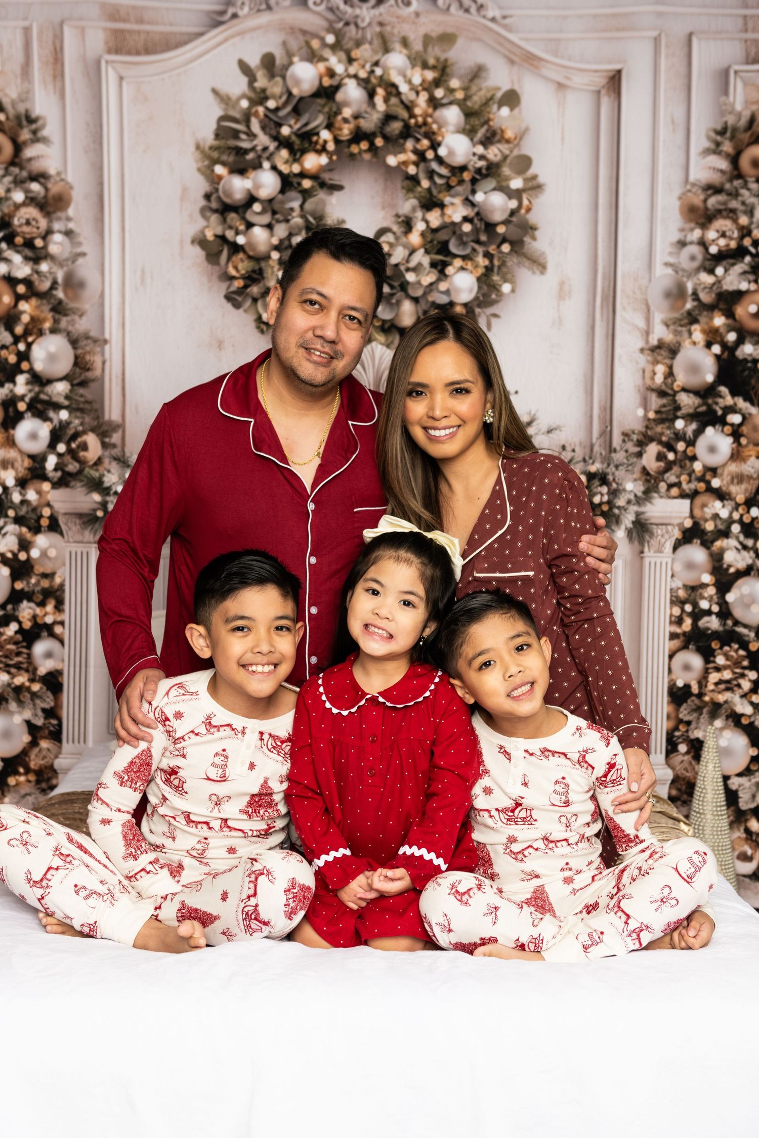 Family Christmas portrait with matching pajamas in front of decorated tree and wreath.