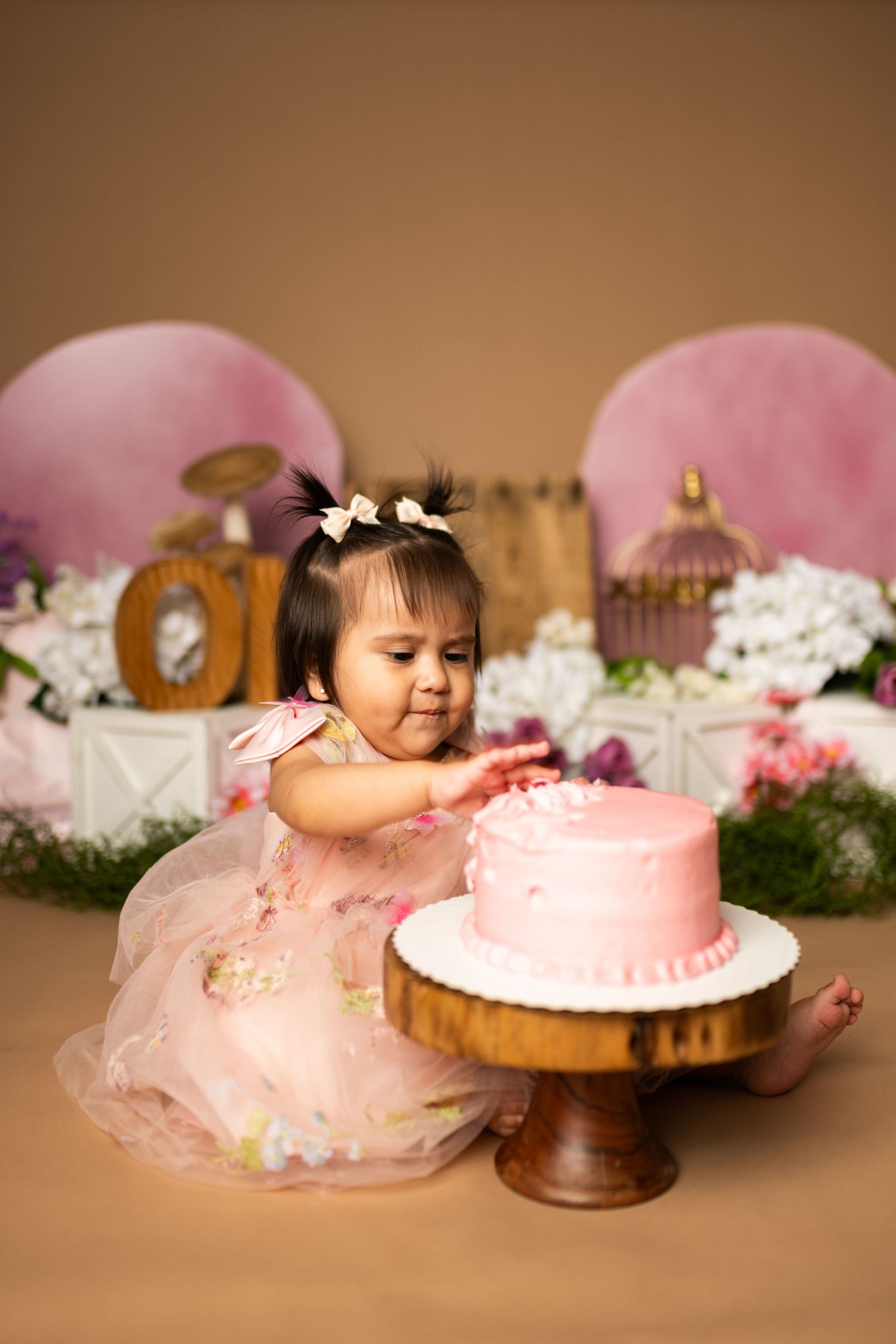 Pink cake smash photography session setup with floral decorations and soft lighting.