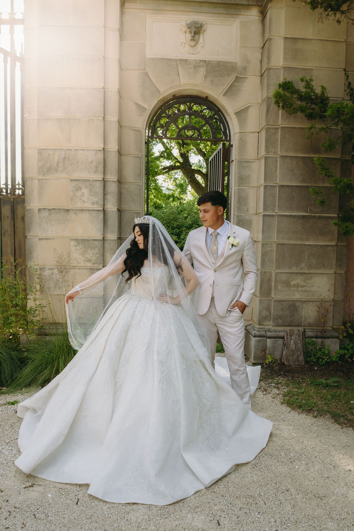Bride and groom in white attire dancing playfully by stone architecture.