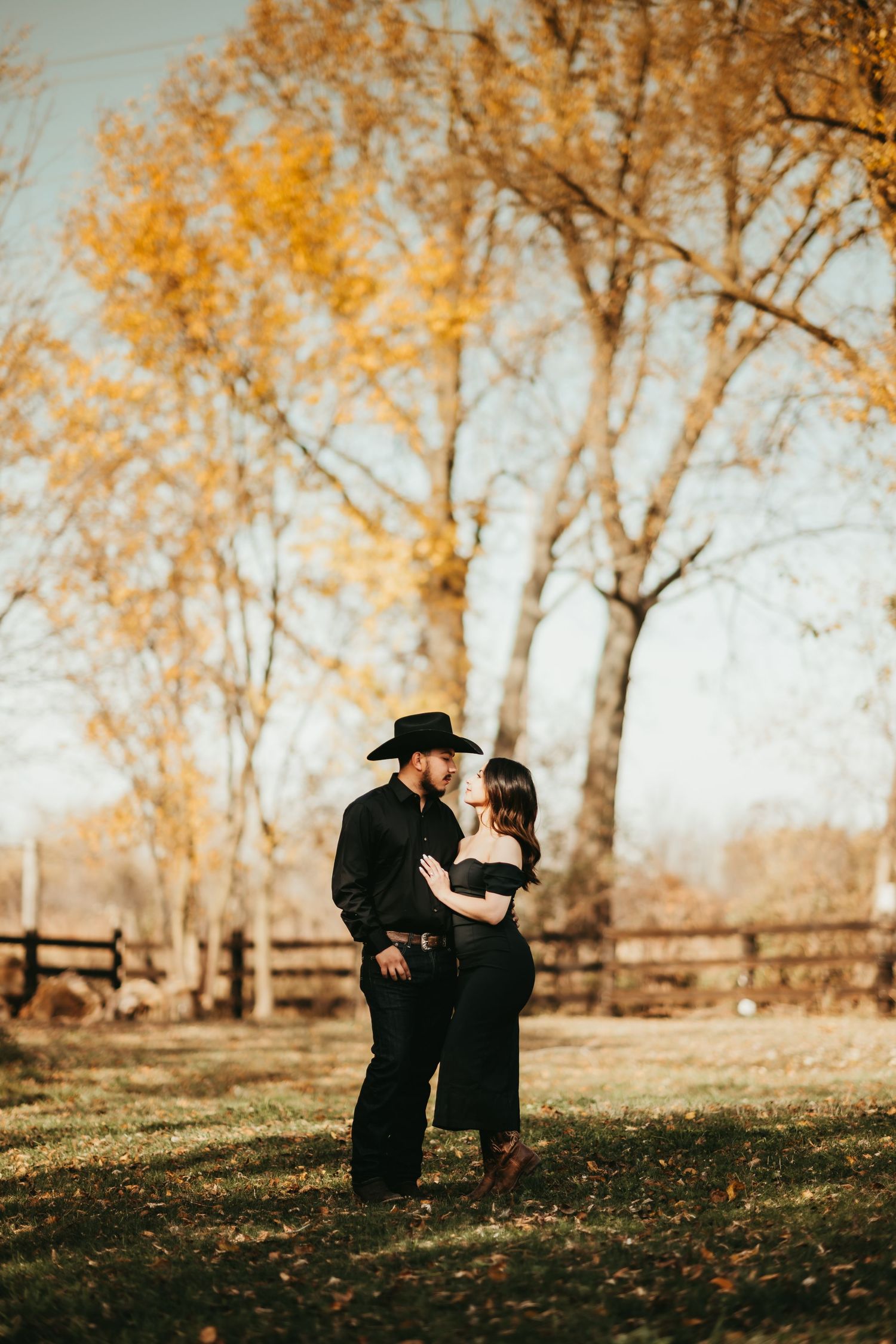 A couple shares romantic moments in a fall setting with golden trees in the background.