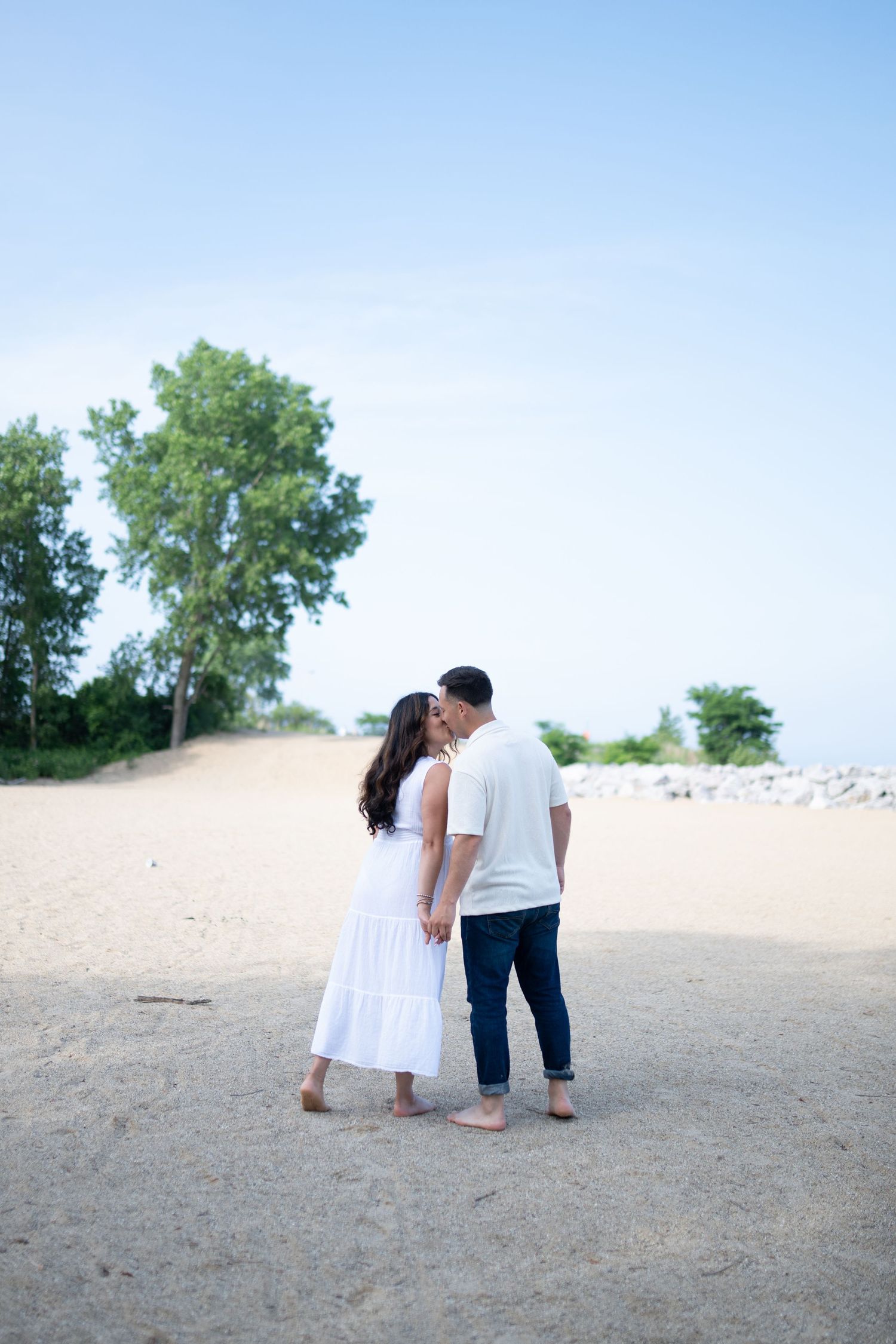 Couple in white outfits sharing intimate moment on sandy beach at sunset.
