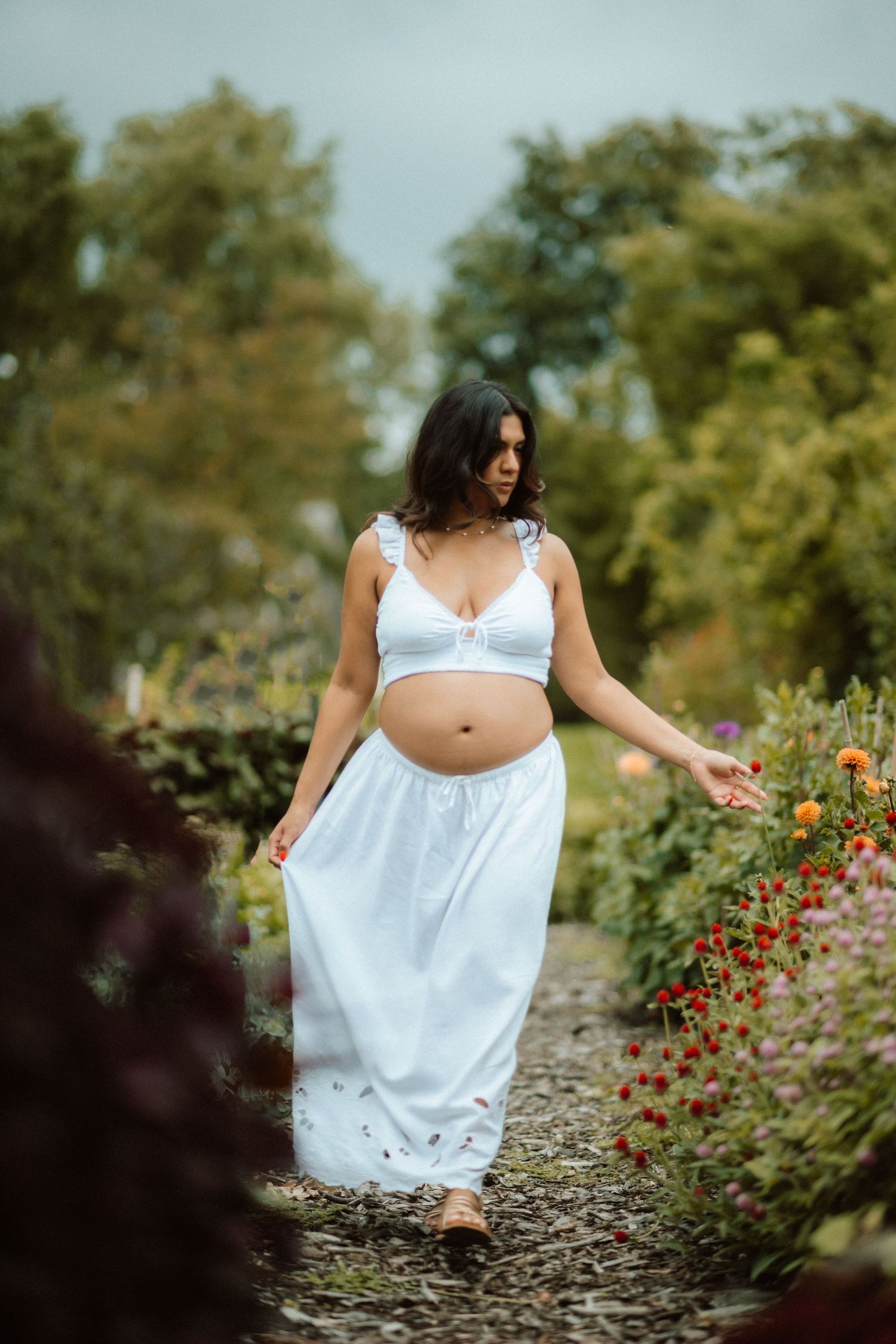 Artistic maternity photos taken in a garden with white dress and red flowers.
