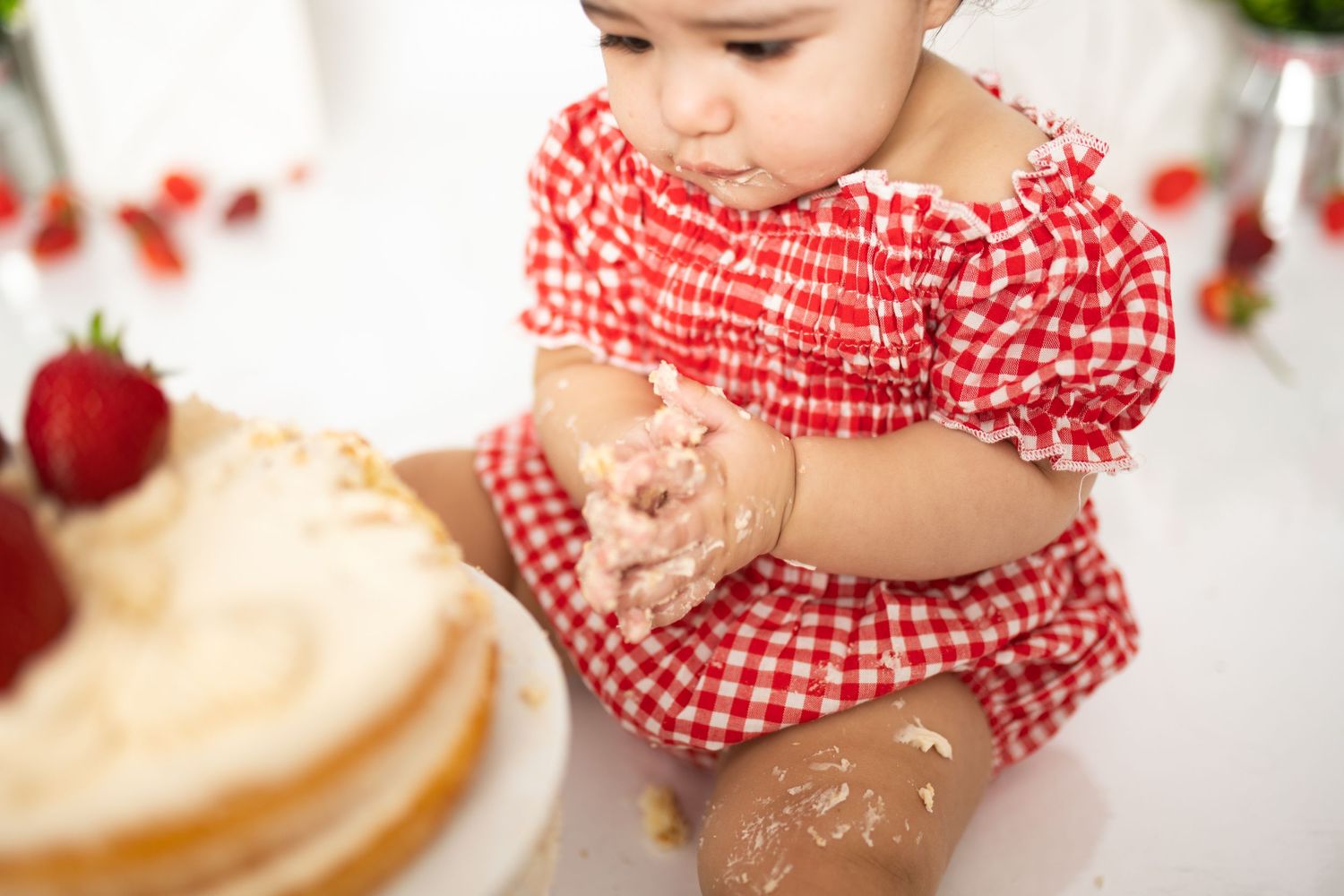 Close-up of baby wearing red gingham outfit during cake smash photoshoot.