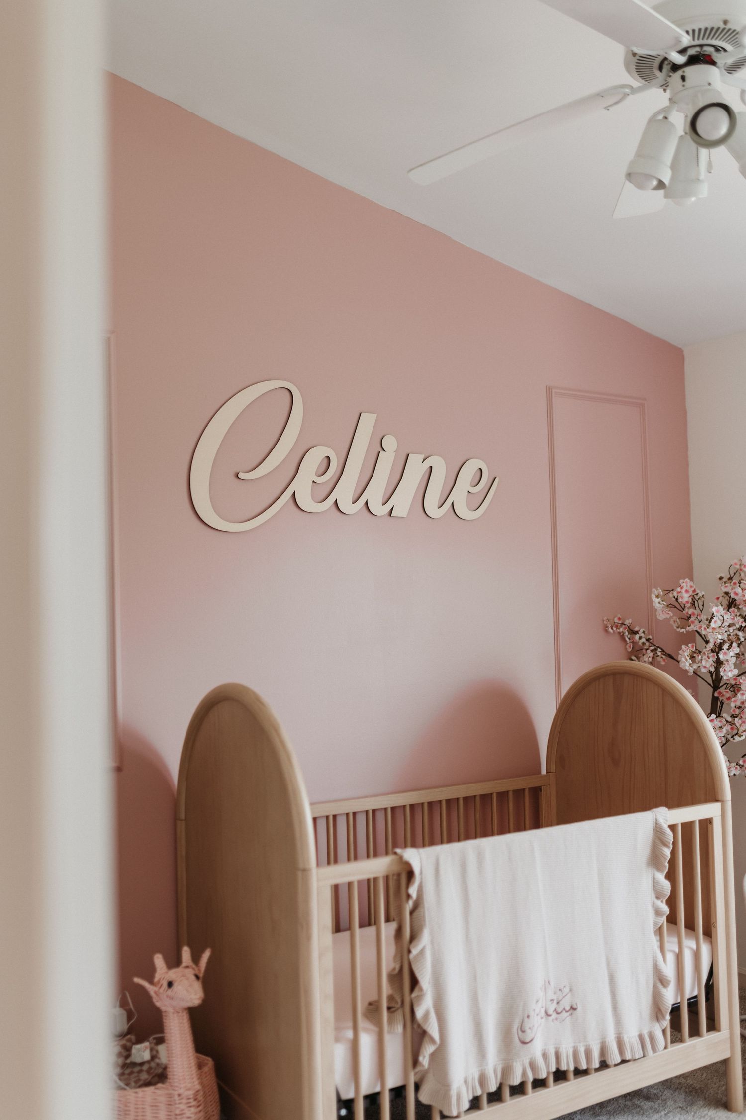 Pink nursery with wooden crib, white ruffled blanket, and cursive 
