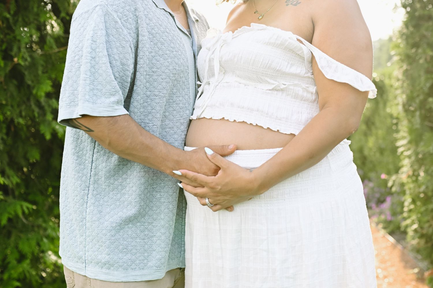 Tender moment captured of expectant couple holding hands in outdoor garden setting.