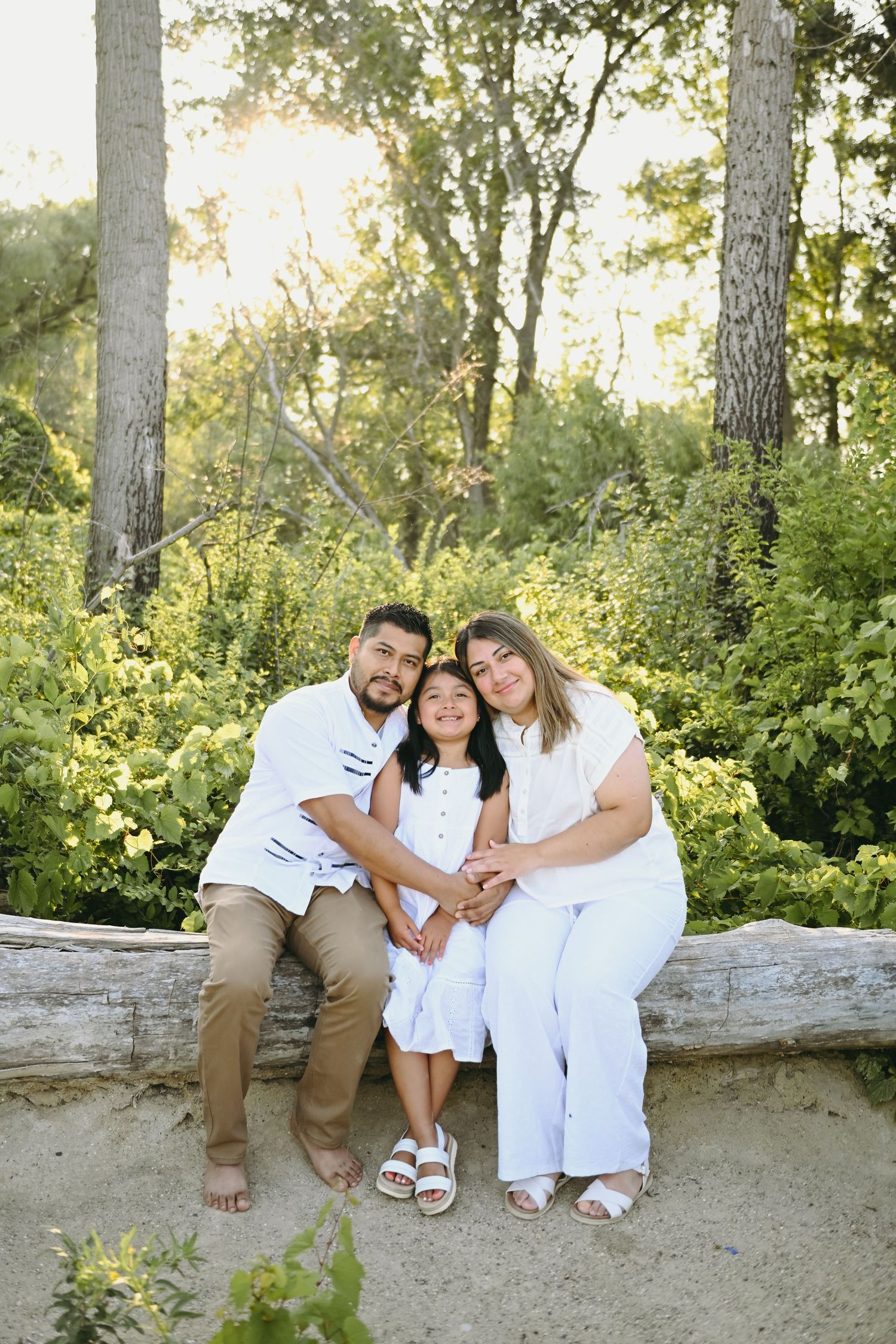 A family sits together on a fallen log during a sunny outdoor photo session.