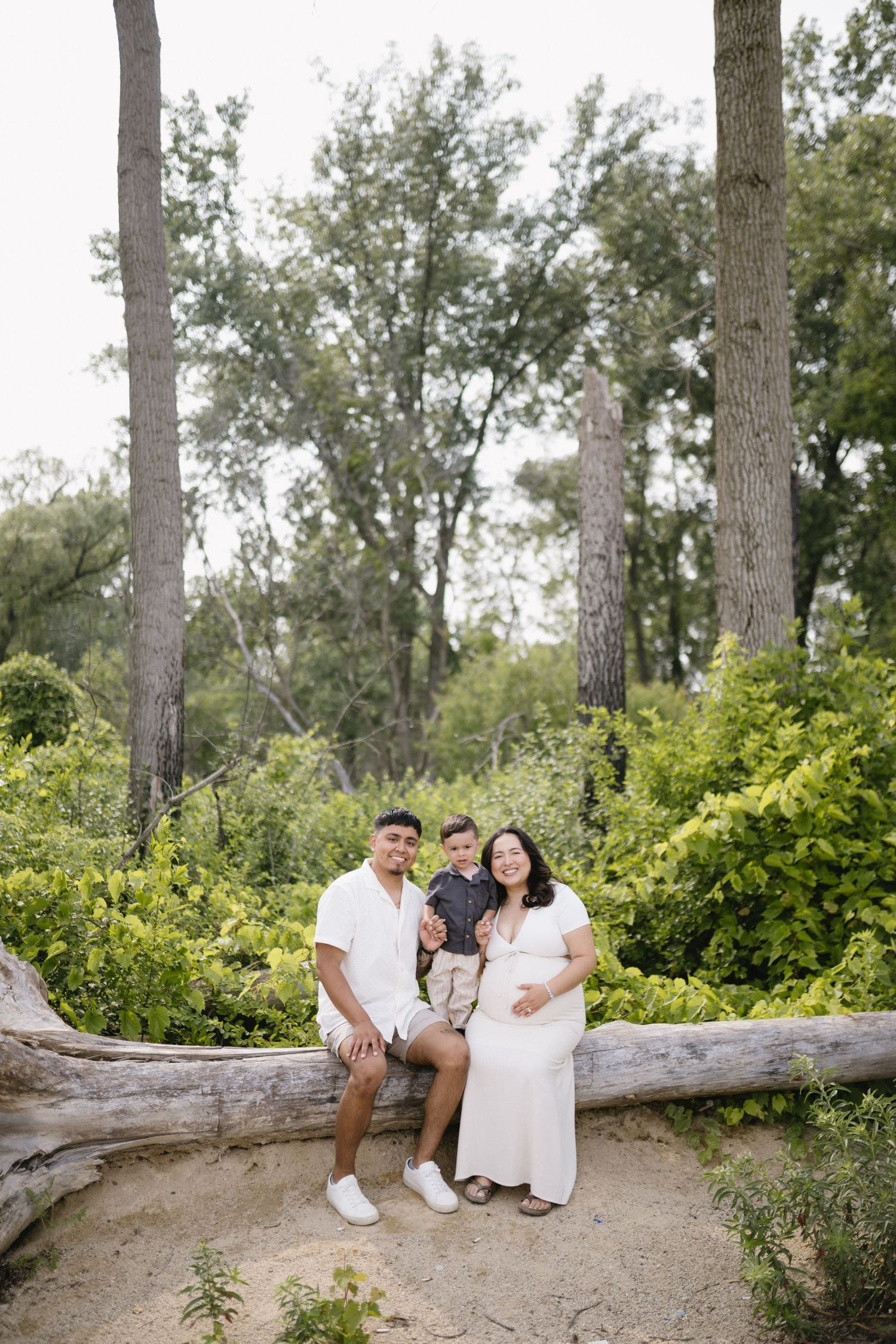 Natural outdoor couple's portrait session on fallen log surrounded by trees.