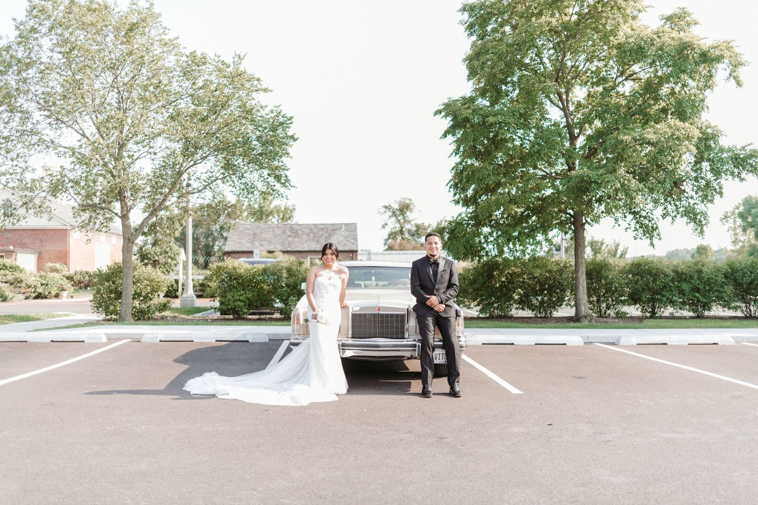 Wedding photography session in an outdoor parking area with trees and buildings in the background.
