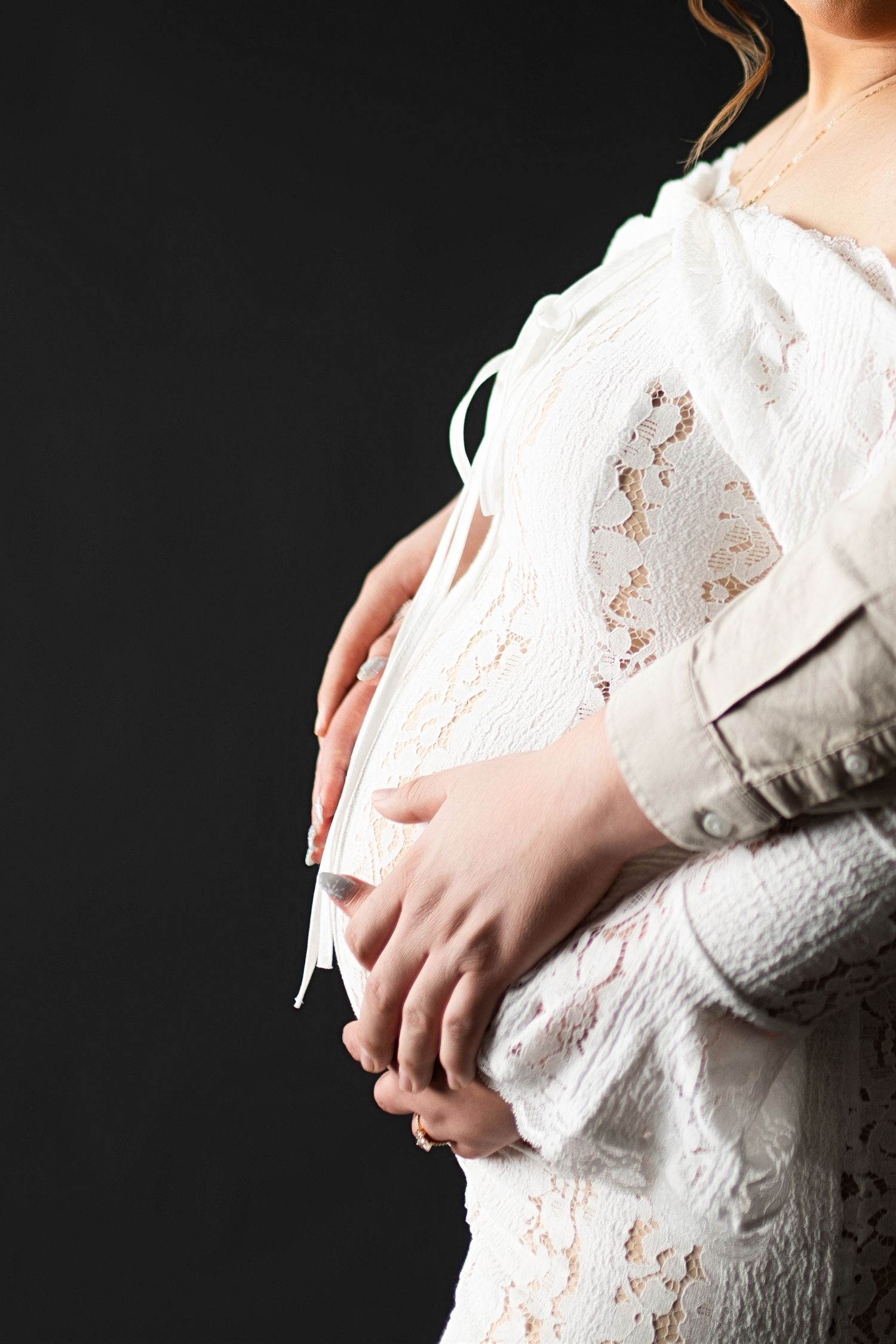 Side view of pregnant woman's belly in white lace dress against dark background.