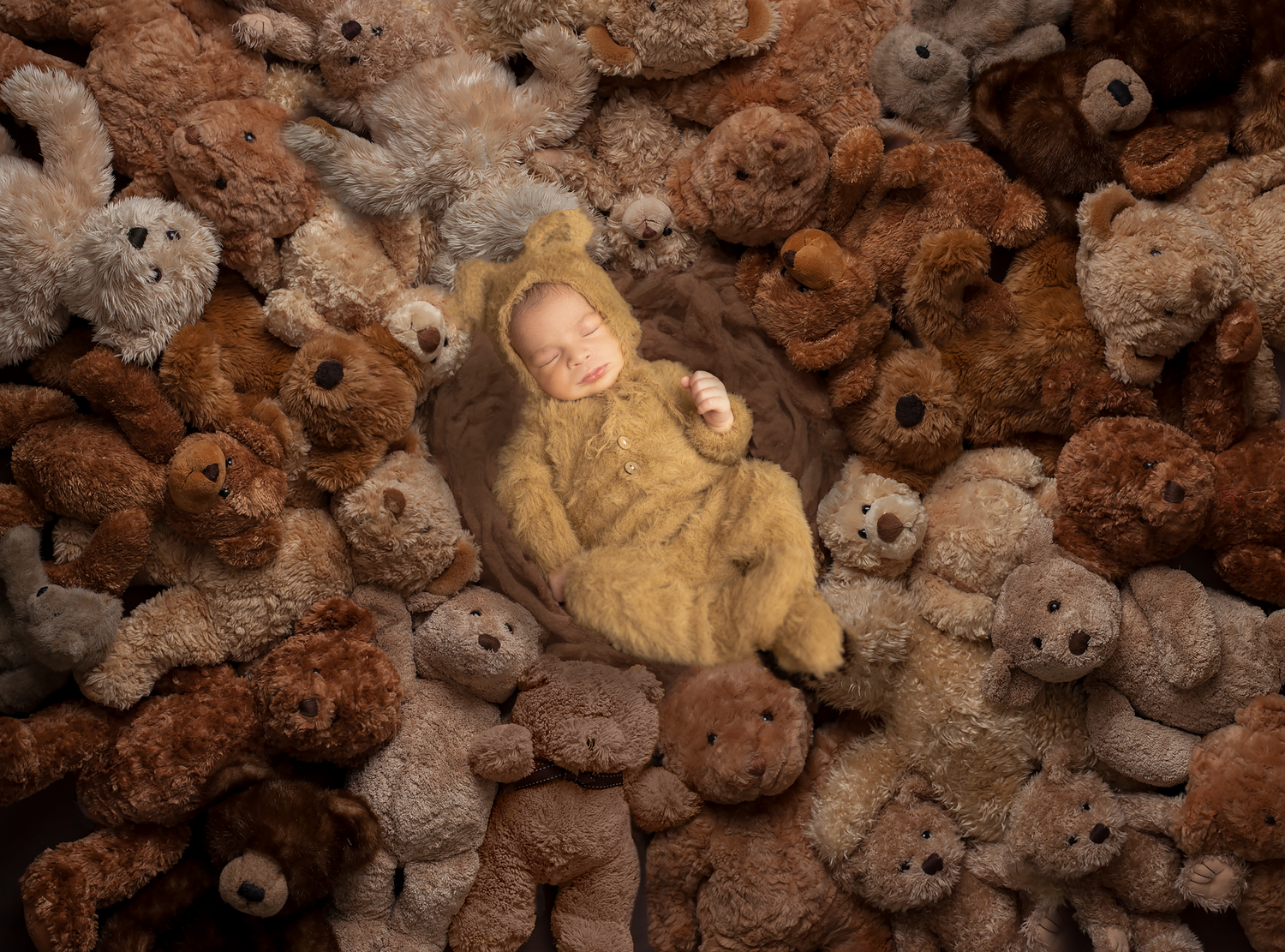 A newborn baby in a yellow knit outfit sleeps peacefully surrounded by a collection of soft brown teddy bears.