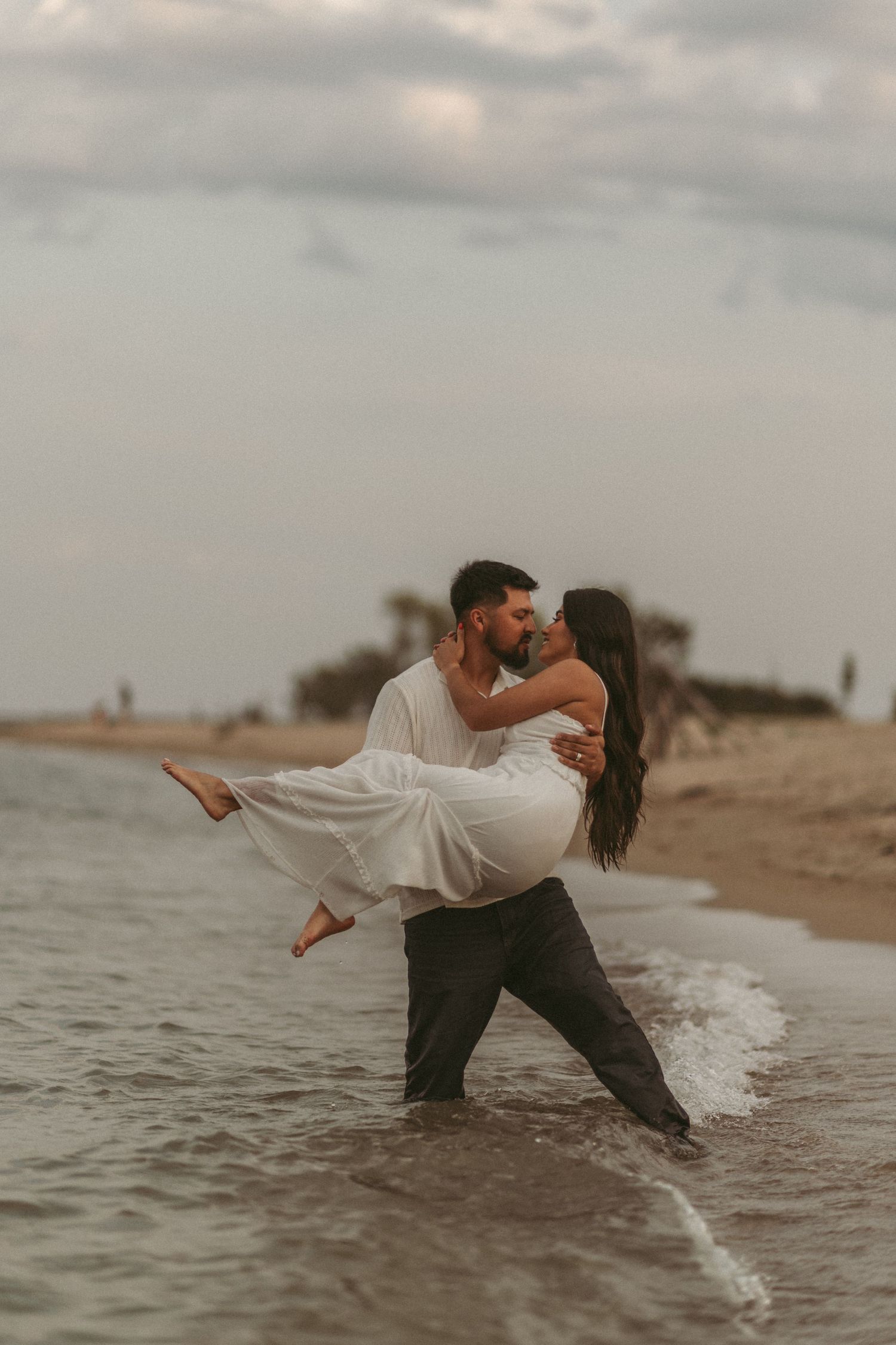 Romantic couple embracing in ocean waves at sunset on beach.