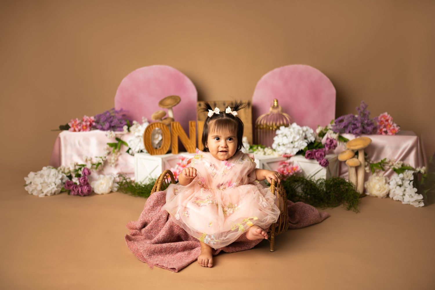 Pink and brown toned first birthday setup with floral decorations and ONE sign.