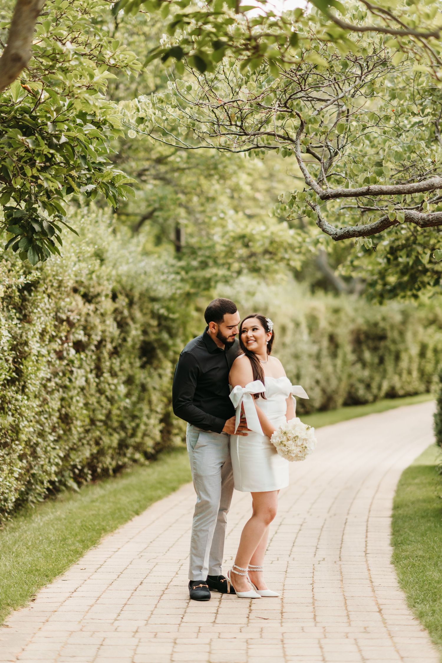 A couple shares tender moments while walking along a winding brick path surrounded by lush greenery.