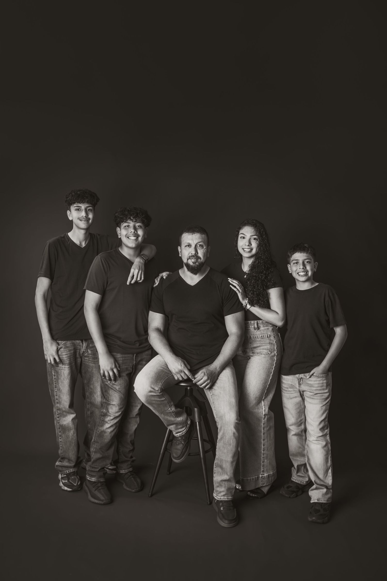 Black and white studio portrait of family group against dark background.