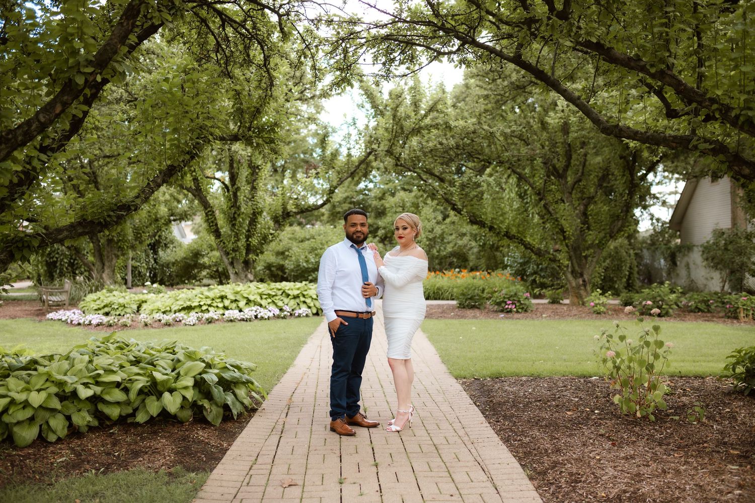 Romantic outdoor couple's photography session on wooden walkway surrounded by gardens.