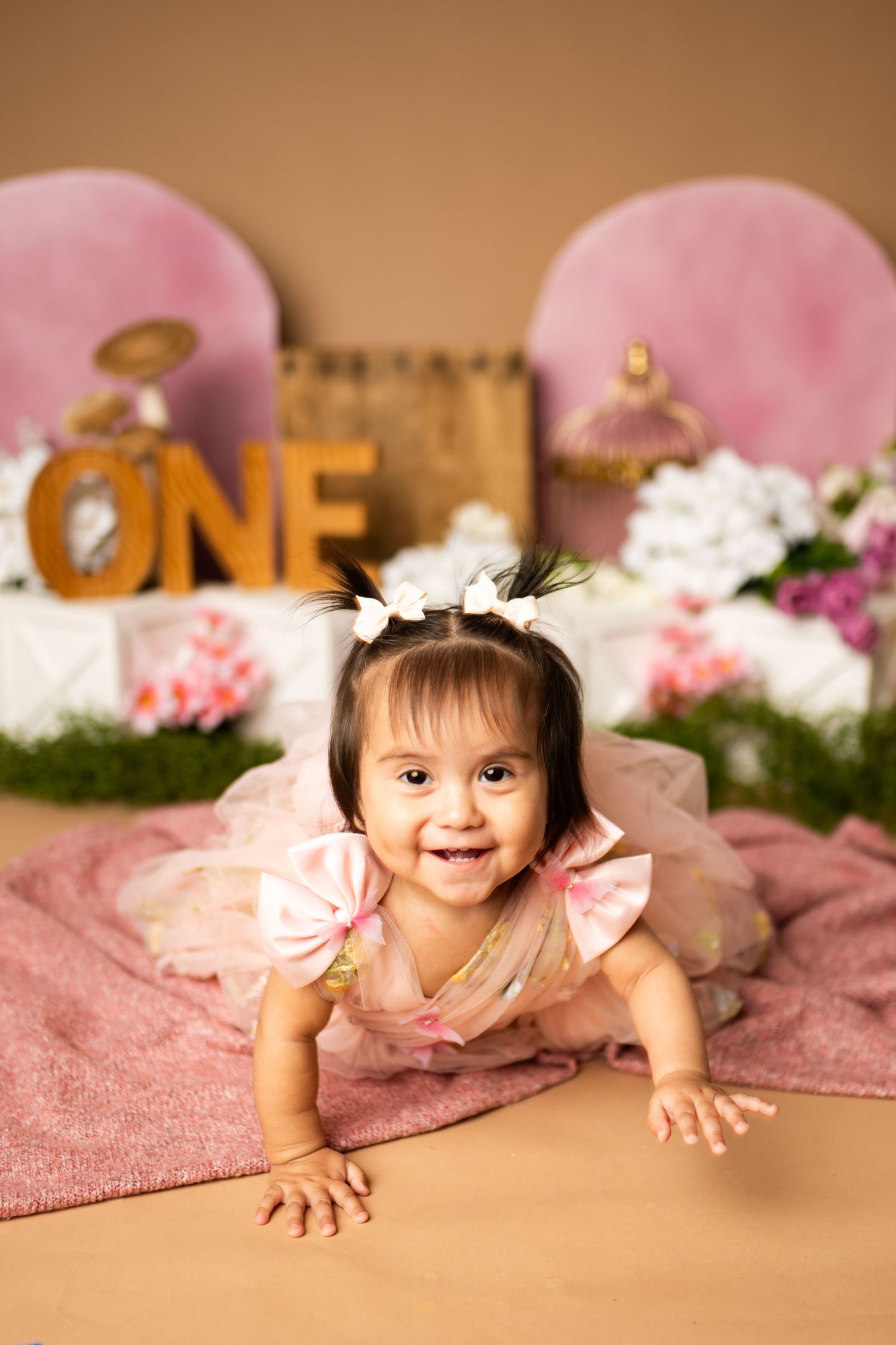 Pink floral first birthday photo setup with baby crawling on textured blanket.