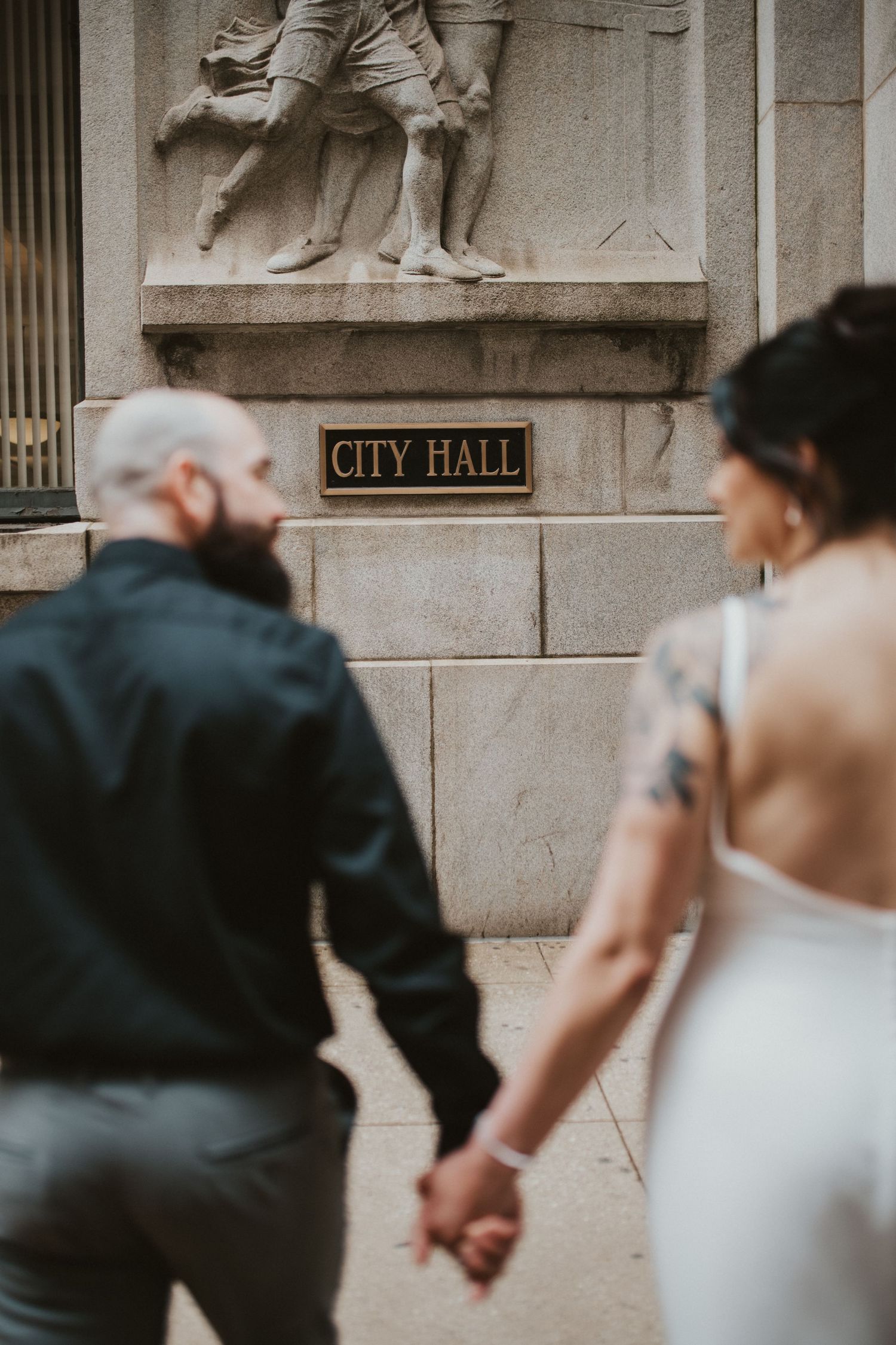Couple holding hands in front of City Hall building with stone relief sculpture.
