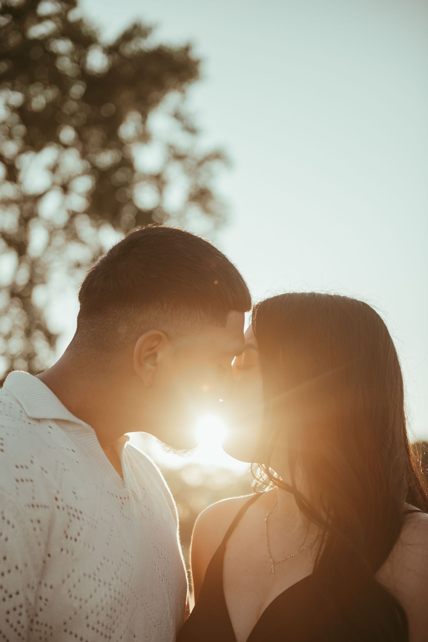 Silhouetted couple shares intimate moment with sun flare between them at sunset.