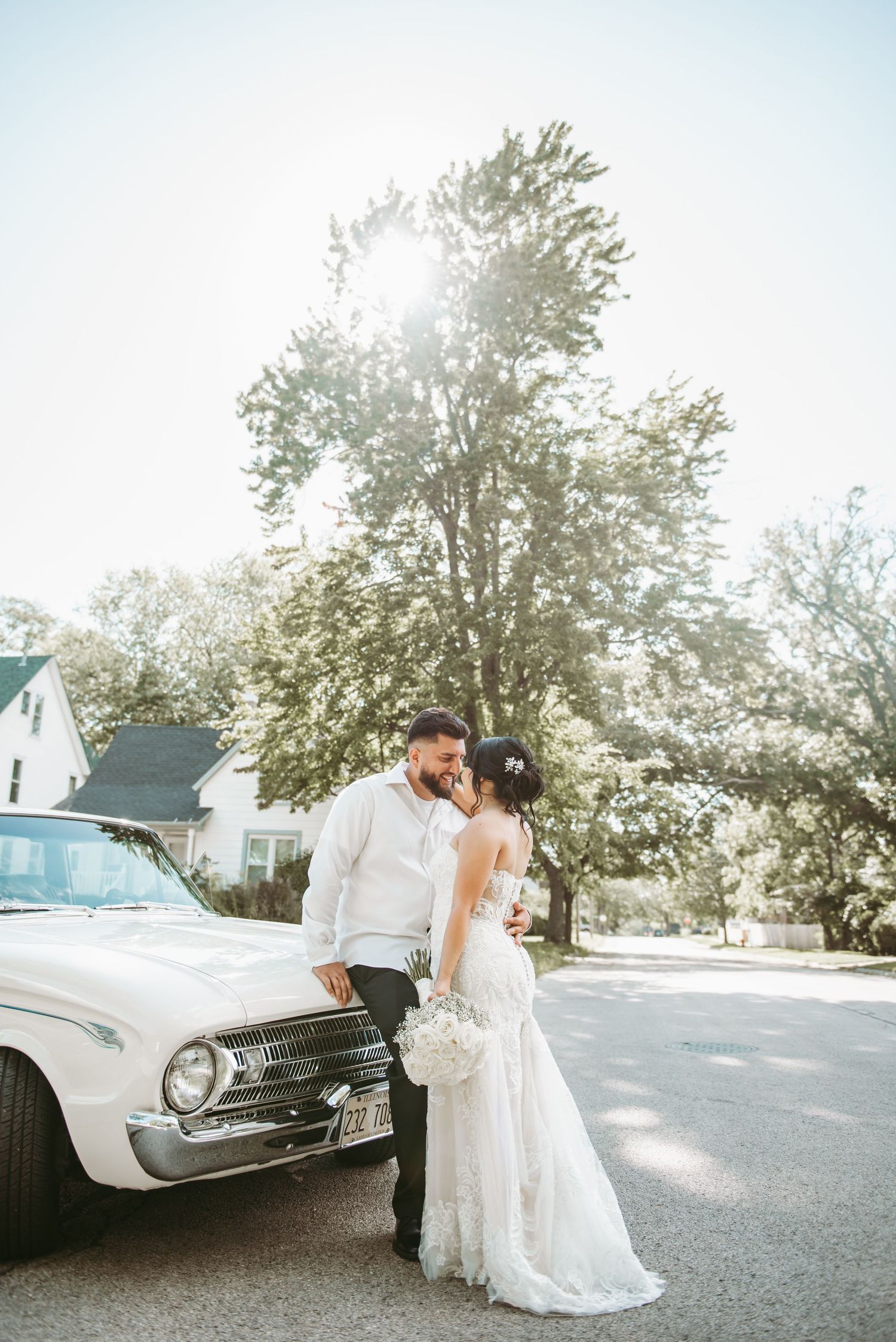 A couple embraces beside a classic car during a bright, sunlit photoshoot.