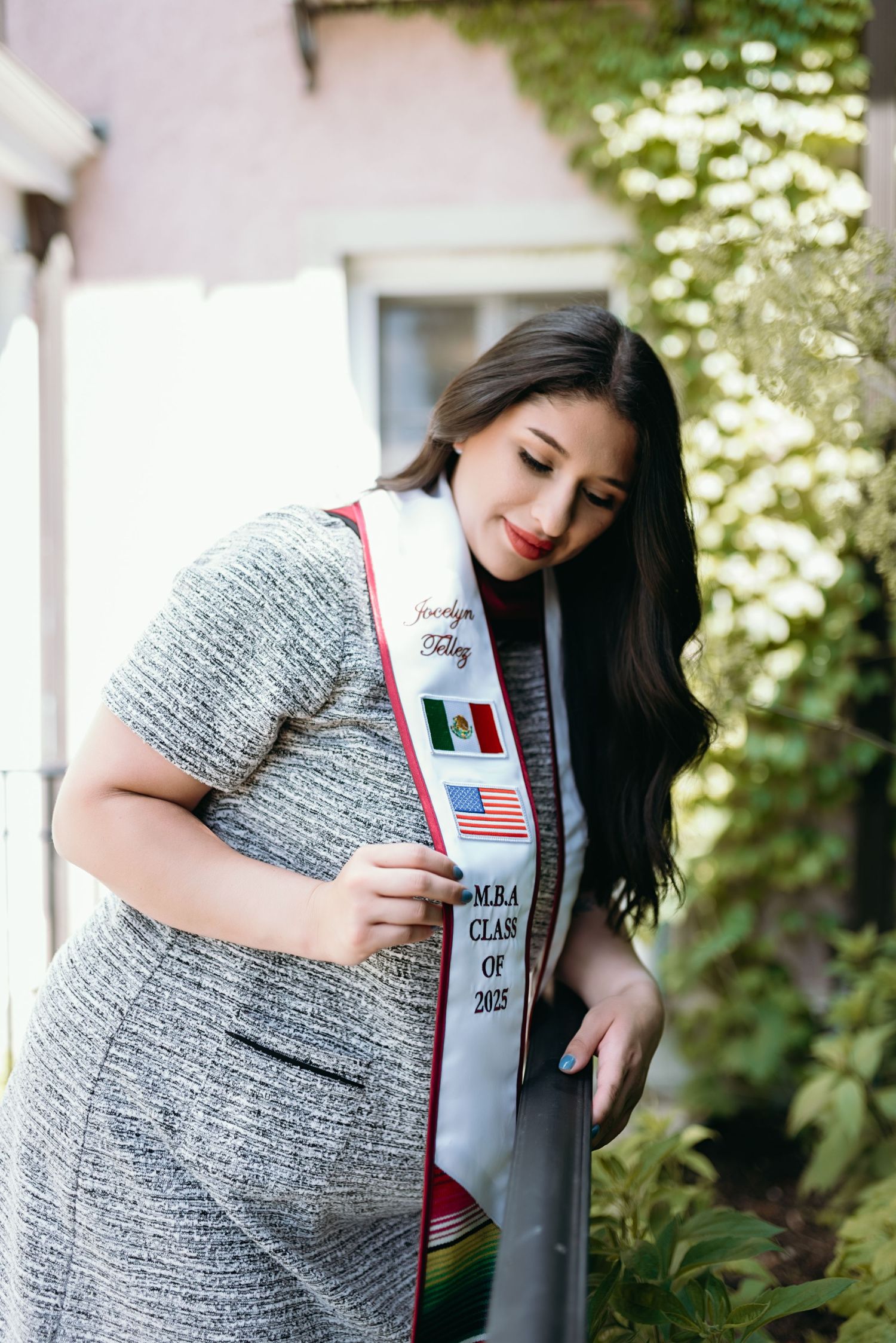 Graduate wearing grey dress with graduation stoles showing flags during outdoor photo shoot.
